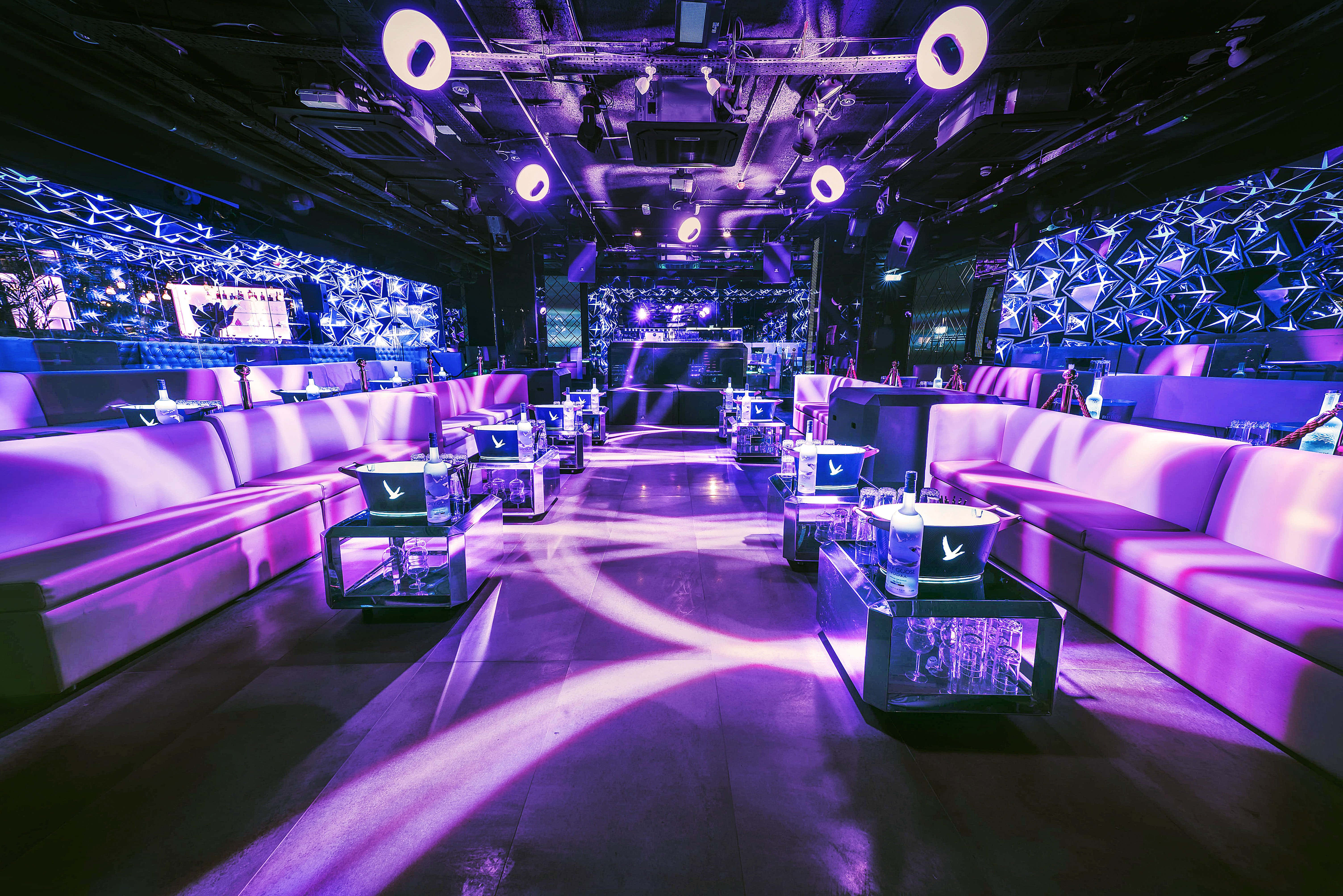 Nightclub 桌布 壁紙 — 一間未來風格的夜總會，發光的紫色燈光映照在時尚沙發和幾何牆面圖案上。