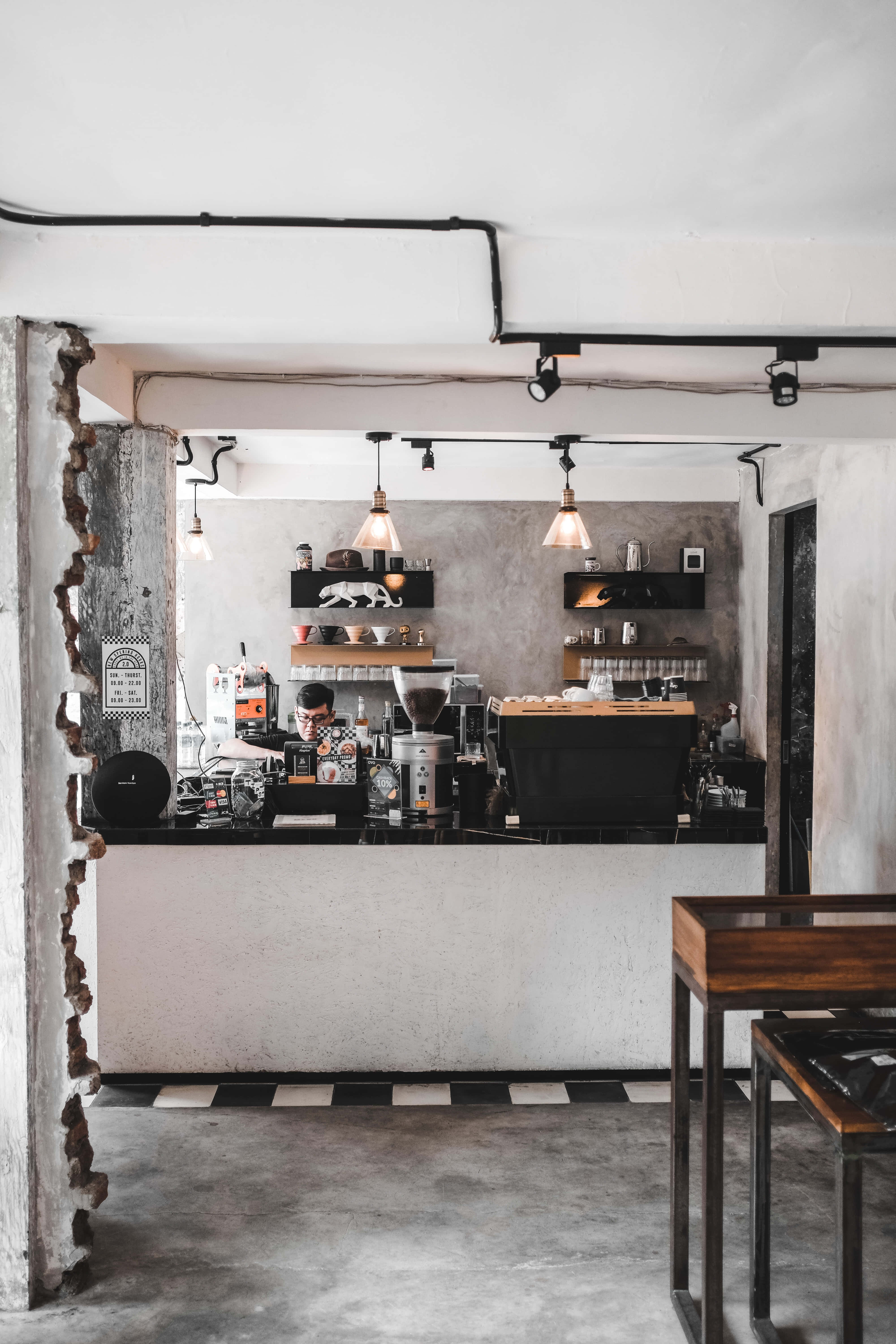 Coffee Aesthetic 桌布 壁紙 — 一間極簡工業風咖啡店，擁有裸露的混凝土牆、黑白棋盤格地板，以及吧台上方溫暖的吊燈。