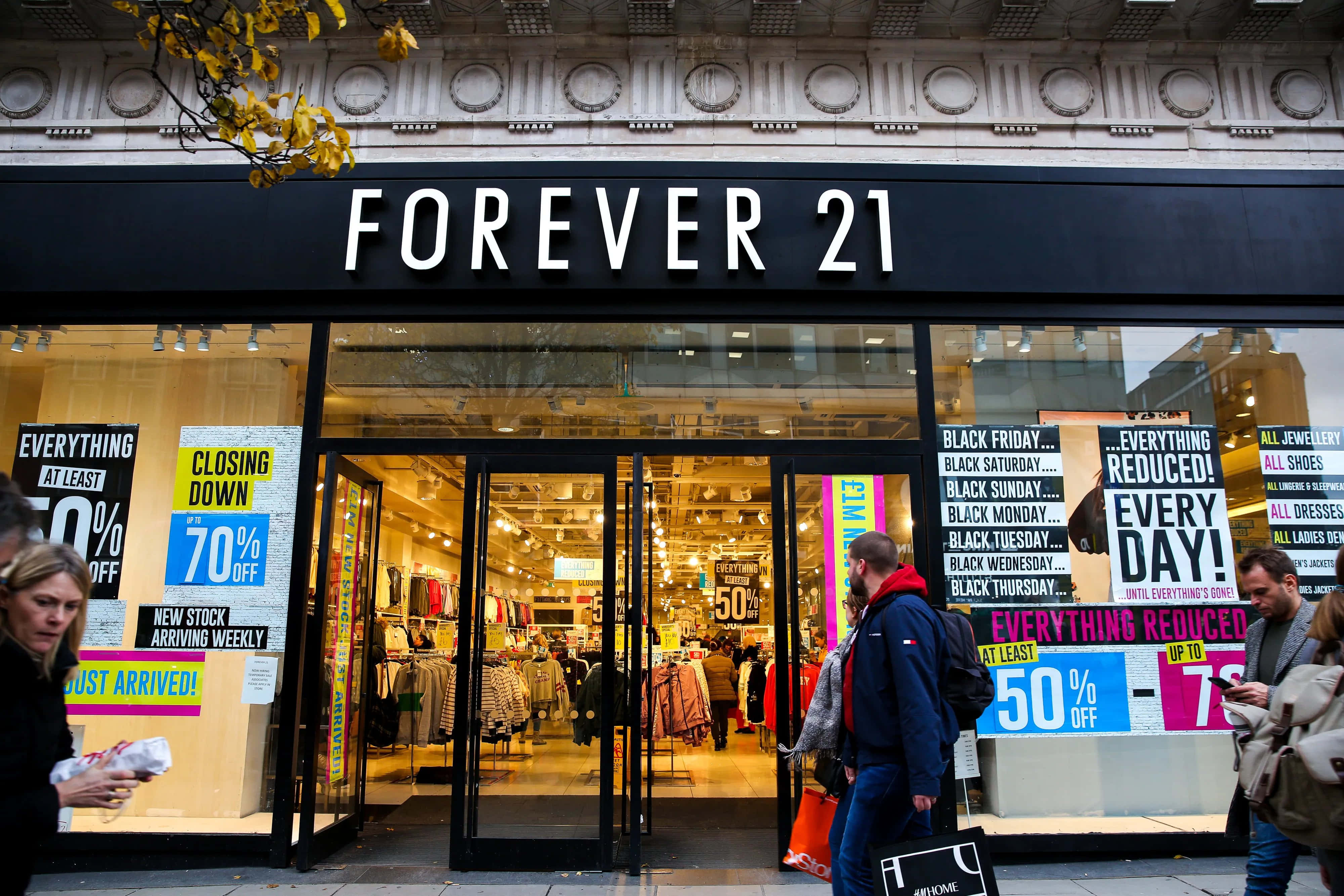 永遠21 桌布 壁紙 — 一間熙熙攘攘的Forever 21商店，帶有醒目的減價標誌和購物者走過其玻璃門。
