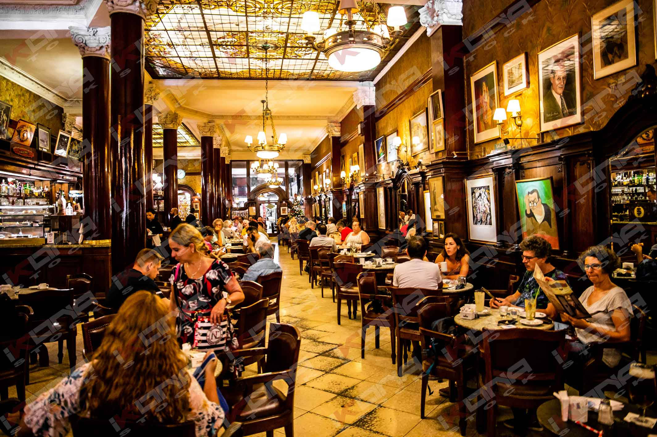 Buenos Aires 桌布 壁紙 — 一間熱鬧的復古餐廳，顧客在華麗吊燈下用餐，牆上掛著鑲框肖像畫，襯托著豐富的木質牆面。