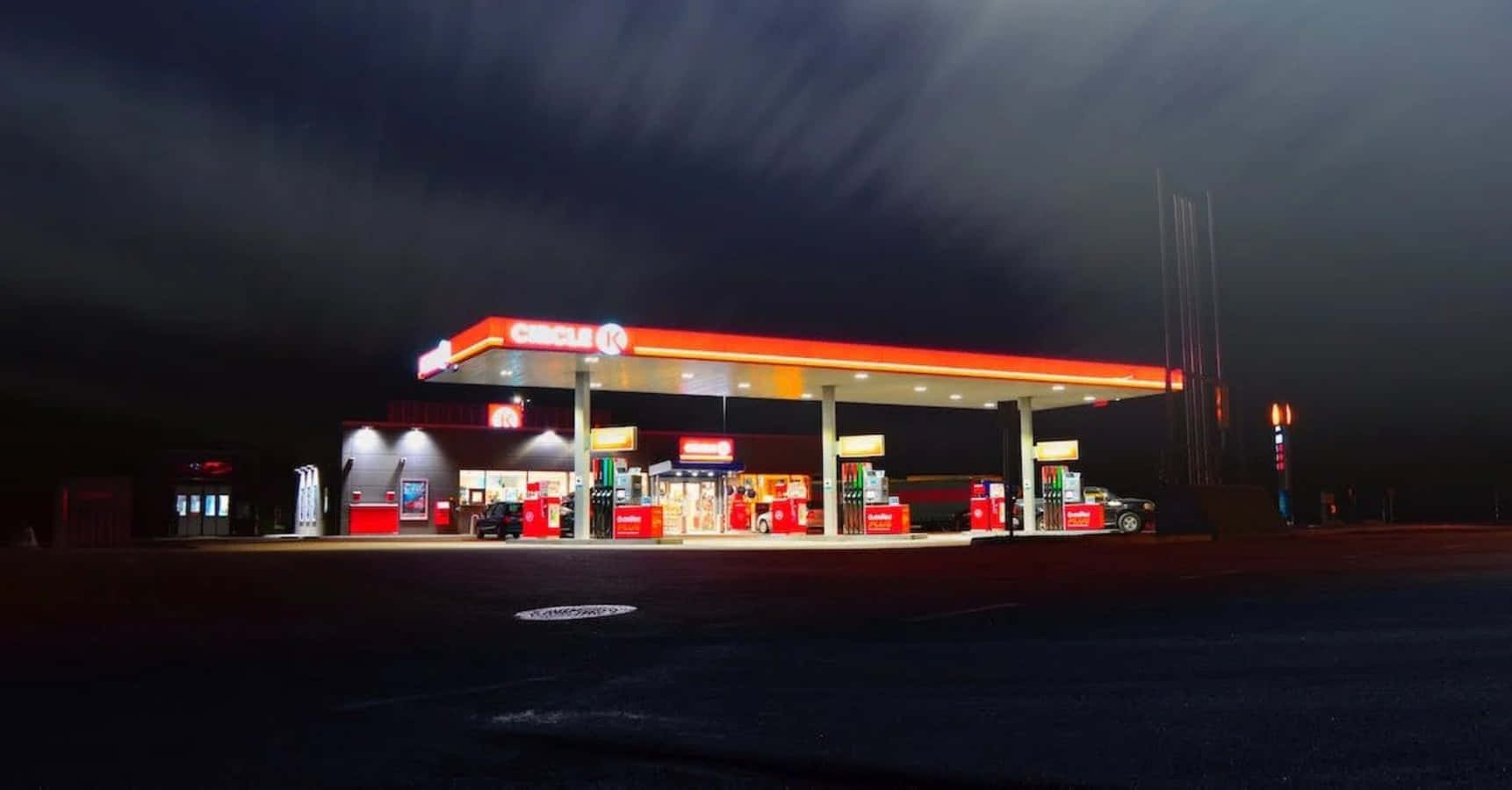 加油站 桌布 壁紙 — 一間燈火通明的Circle K加油站，在陰暗多雲的夜空下閃耀，一輛孤獨的汽車停在油泵旁。