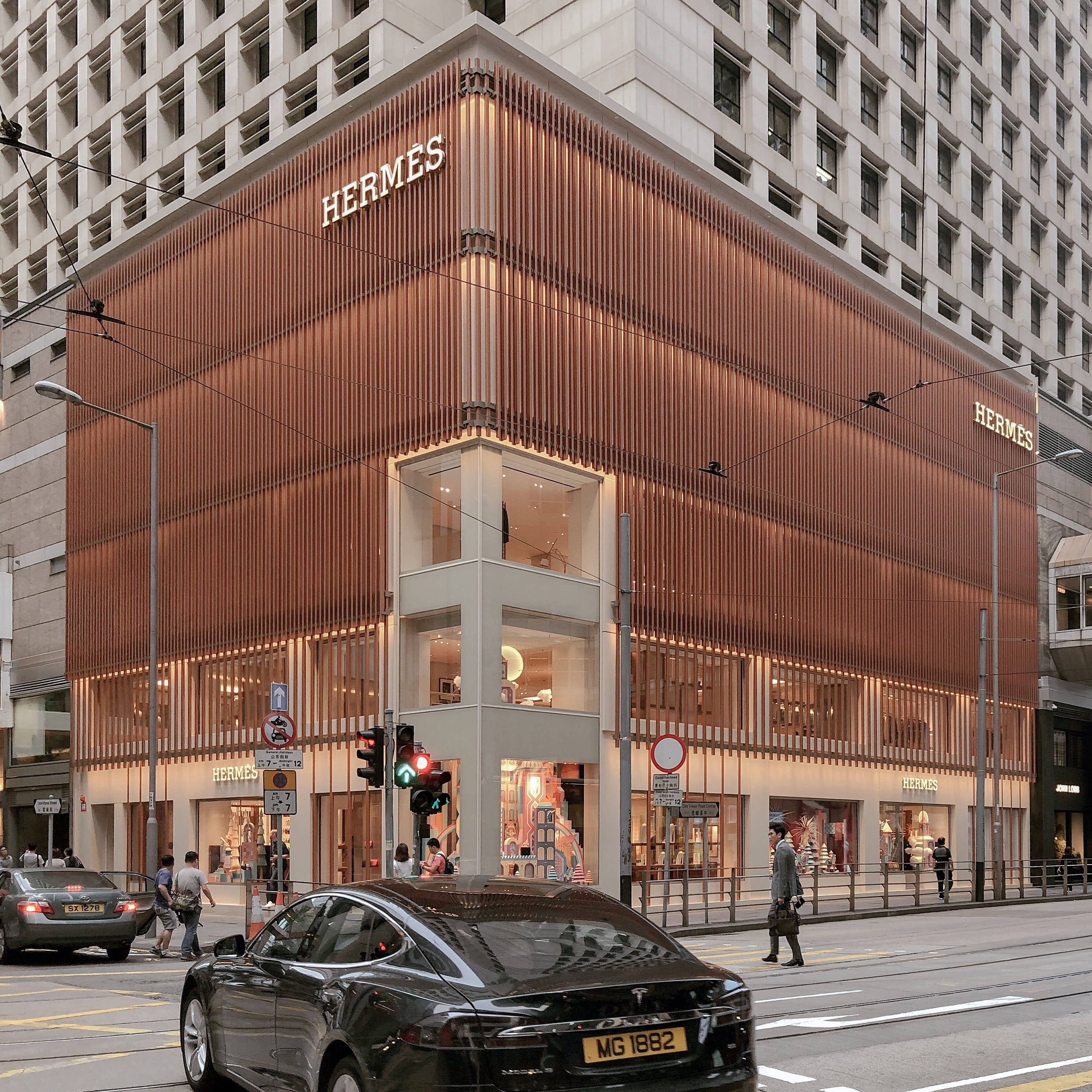 Hermes 桌布 壁紙 — 一間現代 Hermès 旗艦店，帶有銅色垂直板條和發光窗戶，位於繁忙的街角。