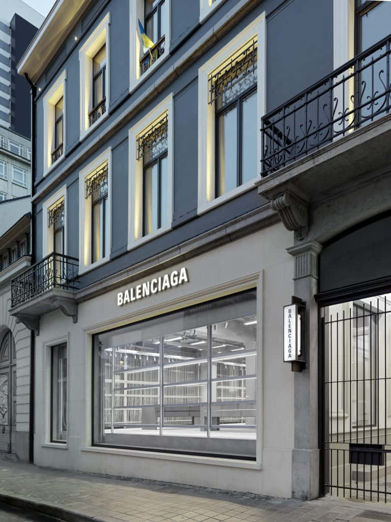 巴黎世家 桌布 壁紙 — 一間現代化的 Balenciaga 精品店，灰色外牆和發光的窗戶，矗立在黃昏的城市街道上。