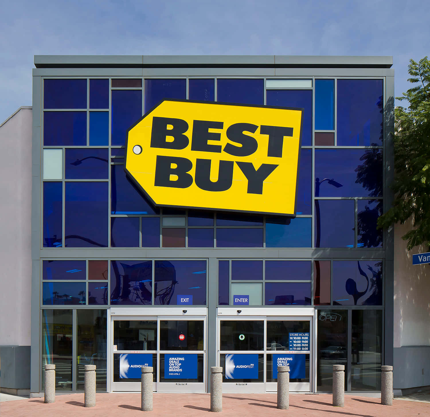 Best Buy 桌布 壁紙 — 一間現代化的Best Buy商店，在晴朗天空下，藍色玻璃窗上有大型黃色標籤標誌。