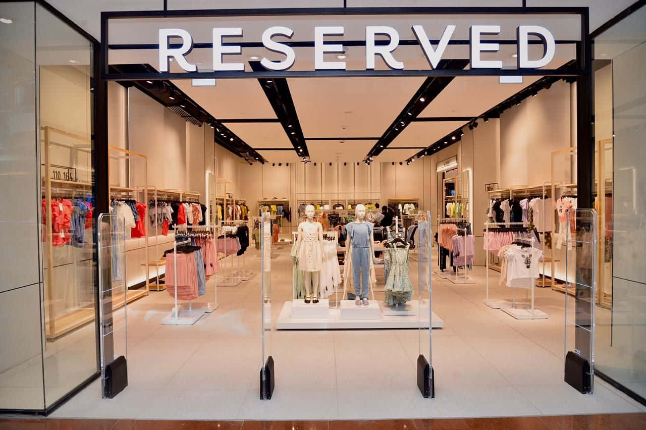 高清 桌布 壁紙 — 一間現代化的Reserved服裝店，設有玻璃門和模特兒，在明亮的頂燈下展示粉彩連衣裙。