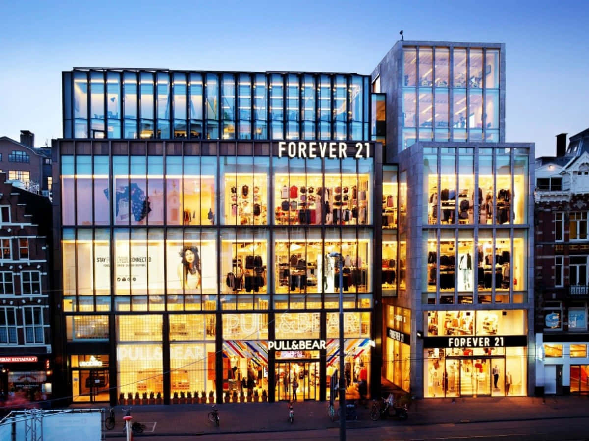 Forever 21 桌布 壁紙 — 一間現代玻璃幕牆的Forever 21和Pull&Bear商店在黃昏時分溫暖地發光，映襯著暮色天空。