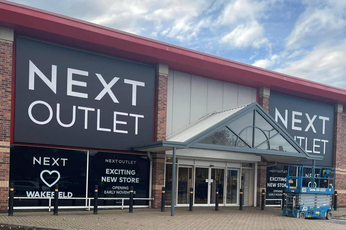 Store 桌布 壁紙 — 一間現代磚牆和玻璃的Next Outlet商店，在部分多雲的天空下設有大膽的招牌。