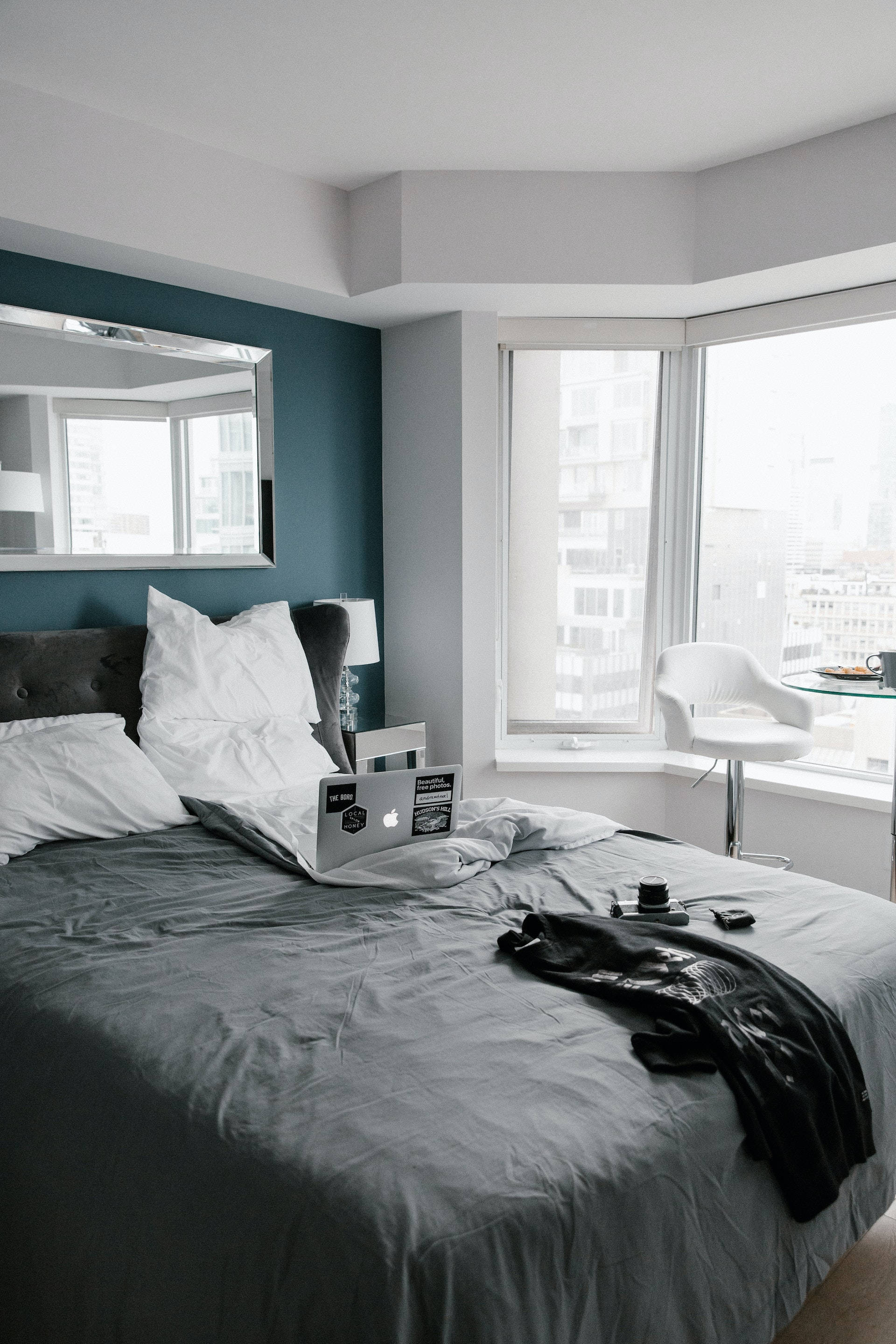 bed 桌布 壁紙 — 一間現代臥室，內有灰色床、筆記型電腦和黑色衣服，透過大窗戶俯瞰城市。