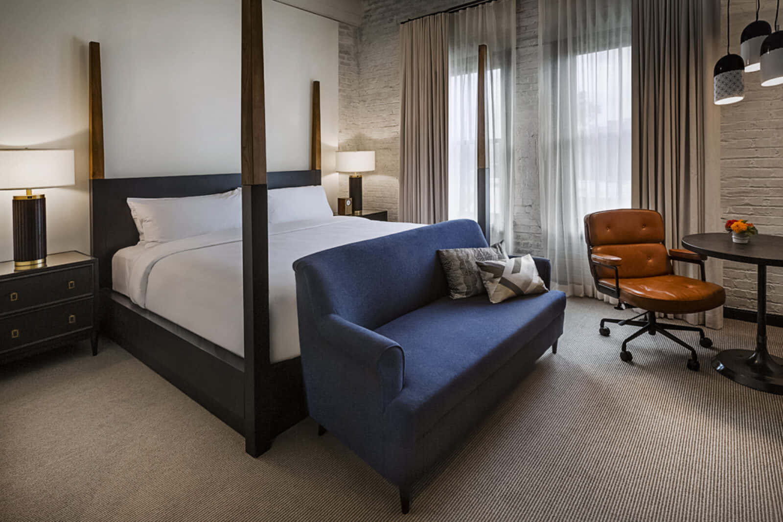 Hotel Room 桌布 壁紙 — 一間現代酒店客房，配備四柱床、藍色沙發、皮革椅子和讓自然光透入的大窗戶。
