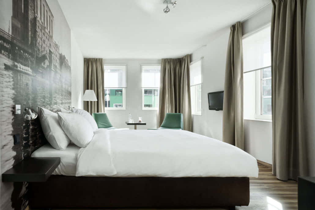 Bedroom 桌布 壁紙 — 一間現代飯店客房，配有一張大床、白色床單、綠色椅子，以及牆上的黑白運河壁畫。