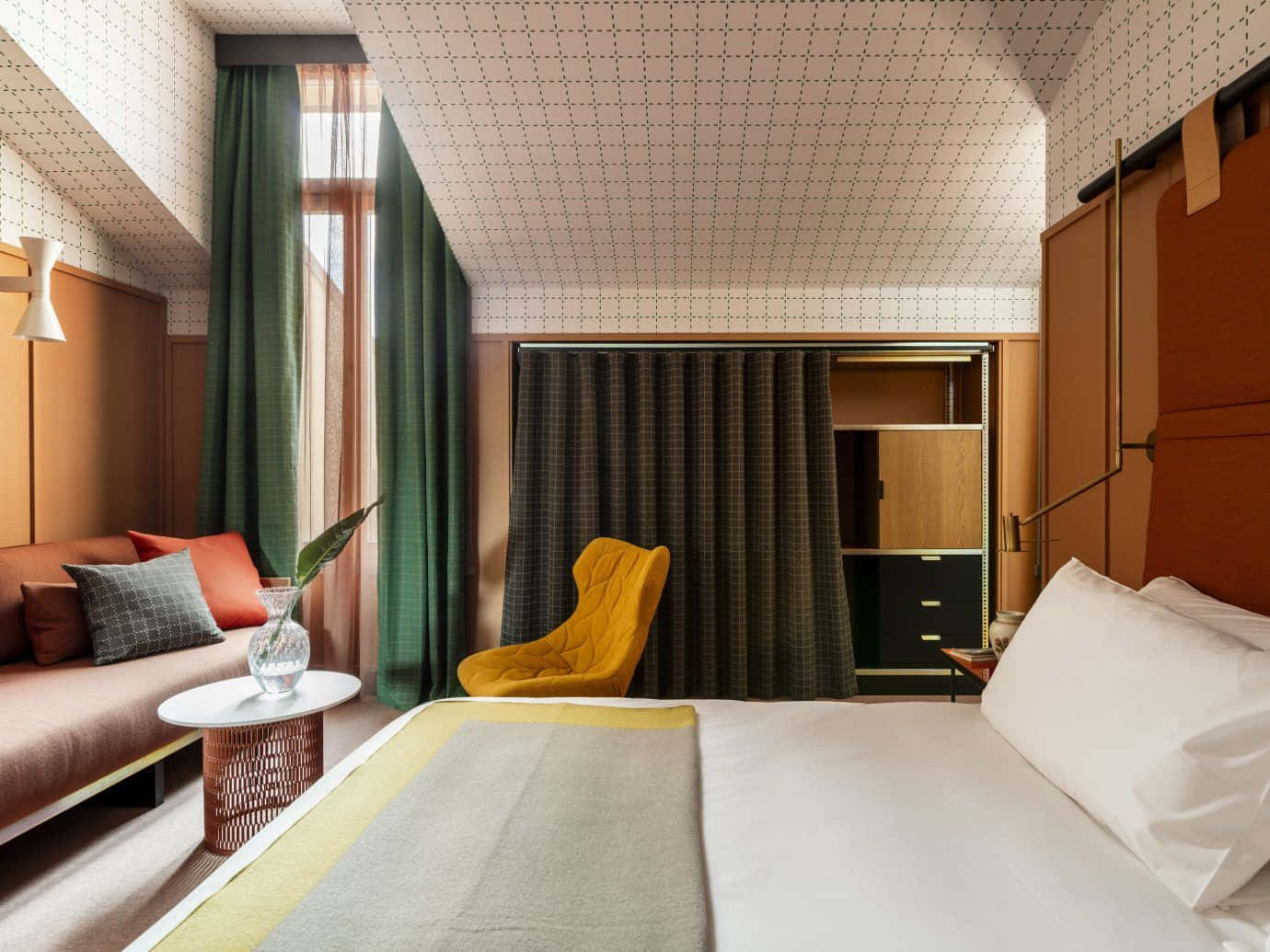 Hotel Room 桌布 壁紙 — 一間現代飯店客房，配有白色床、芥末黃椅子、綠色窗簾和幾何圖案壁紙，在自然光下。