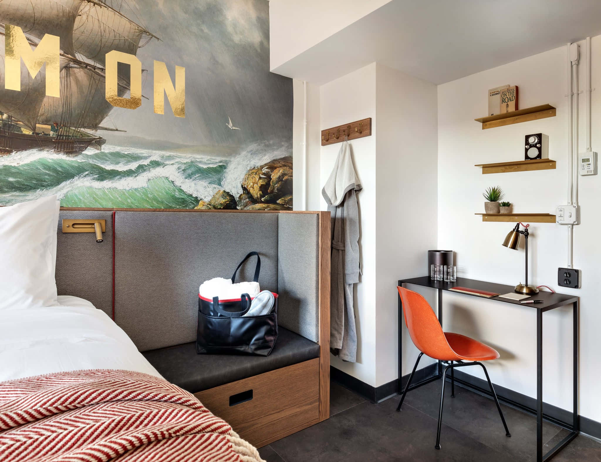 Bedroom 桌布 壁紙 — 一間現代飯店客房設有一張帶紅色圖案毯子的床、橙色椅子，以及一幅帶有金色字母的戲劇性海洋壁畫。