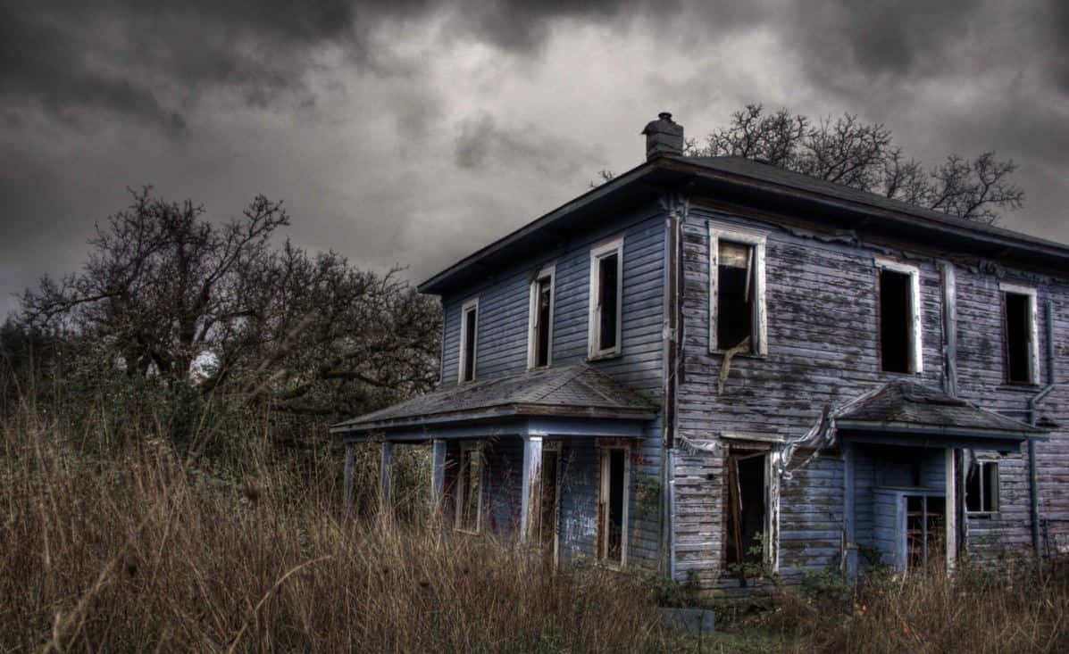 Haunted House 桌布 壁紙 — 一間破舊的藍色房子，窗戶破損，在暴風雨般的灰色天空下被遺棄，周圍長滿了雜草和光禿禿的樹木。