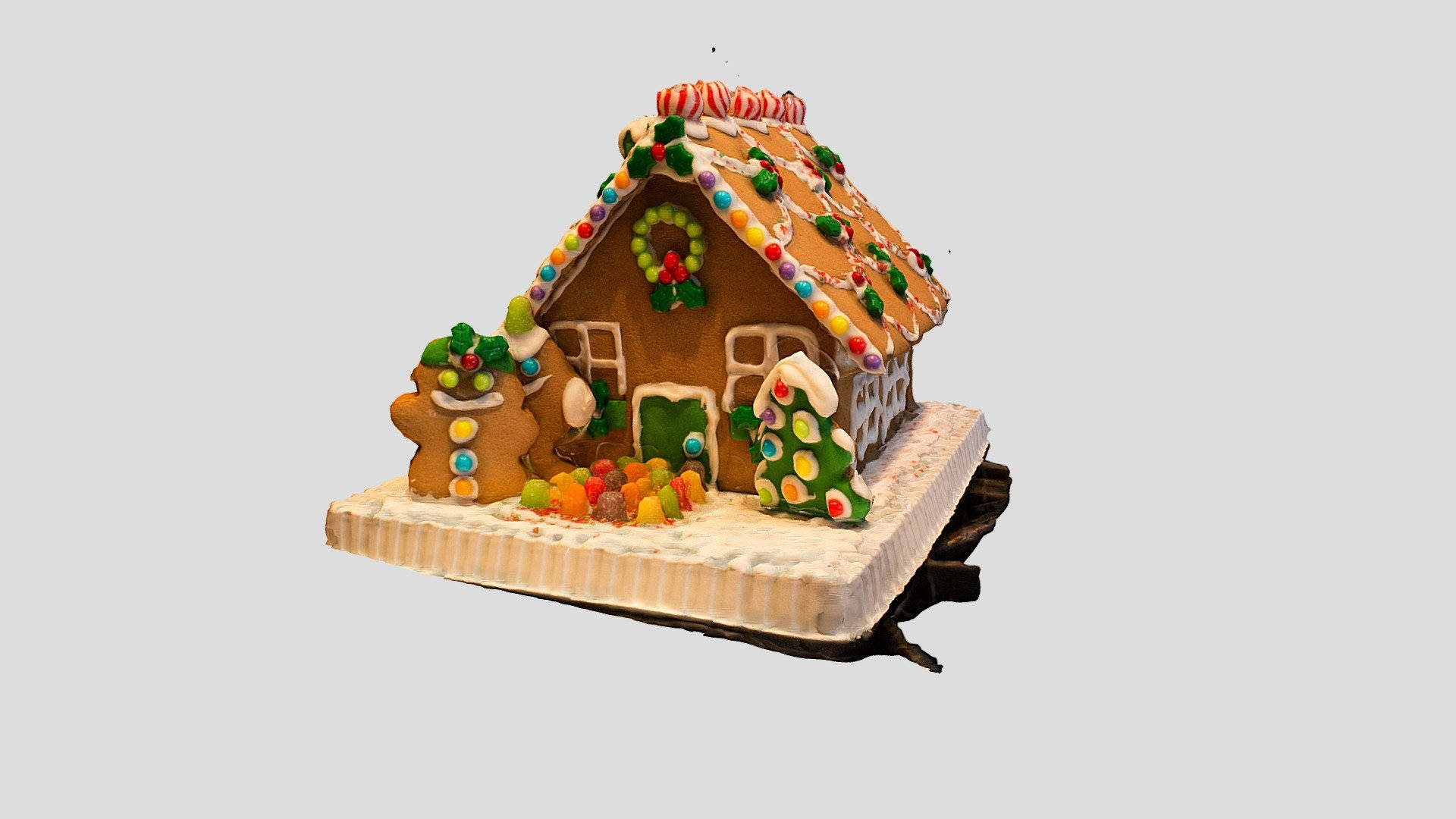 Gingerbread House 桌布 壁紙 — 一間節日薑餅屋，飾有彩色糖果和糖霜，坐落在雪地基座上，附近有薑餅人偶。