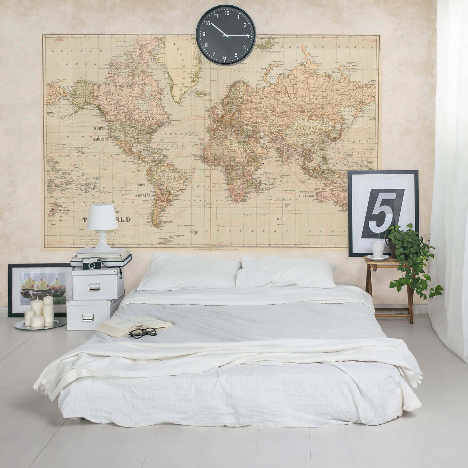 World Map Aesthetic 桌布 壁紙 — 一間簡約風格的臥室，床鋪白色床單，上方是復古世界地圖壁紙和黑色時鐘。