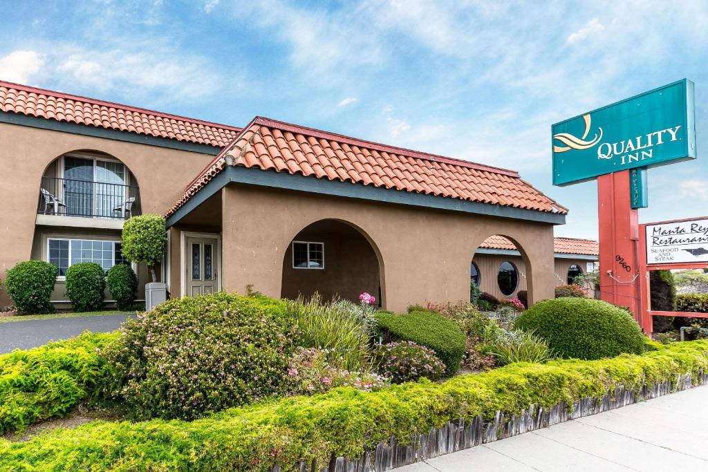 Hotel 桌布 壁紙 — 一間米色灰泥飯店，擁有紅色瓦片屋頂和拱形入口，周圍環繞著修剪整齊的綠色灌木，天空部分多雲，呈現藍色。