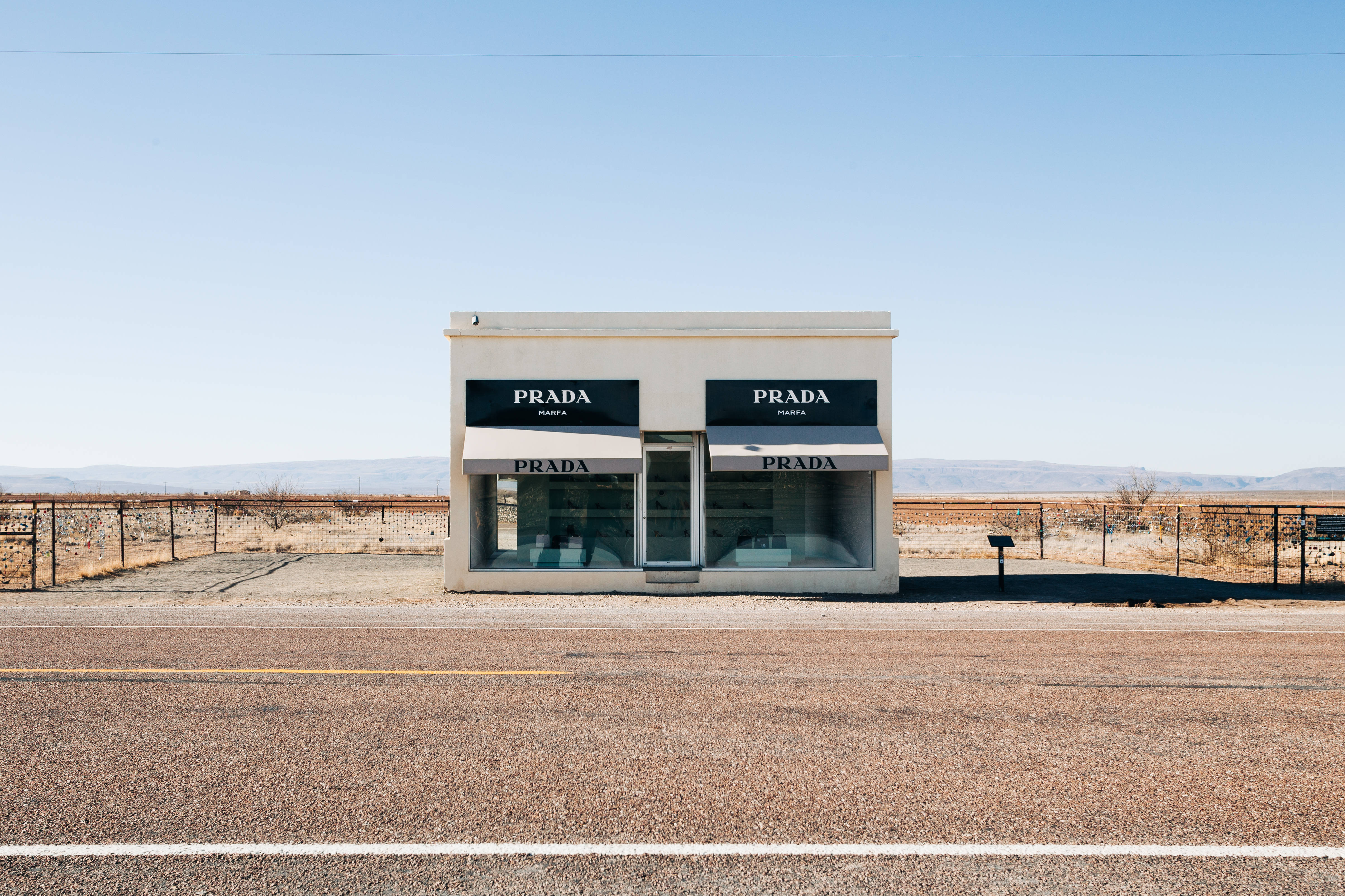 Prada 桌布 壁紙 — 一間純白色的Prada商店孤獨地矗立在晴朗藍天下荒蕪的沙漠景觀中。