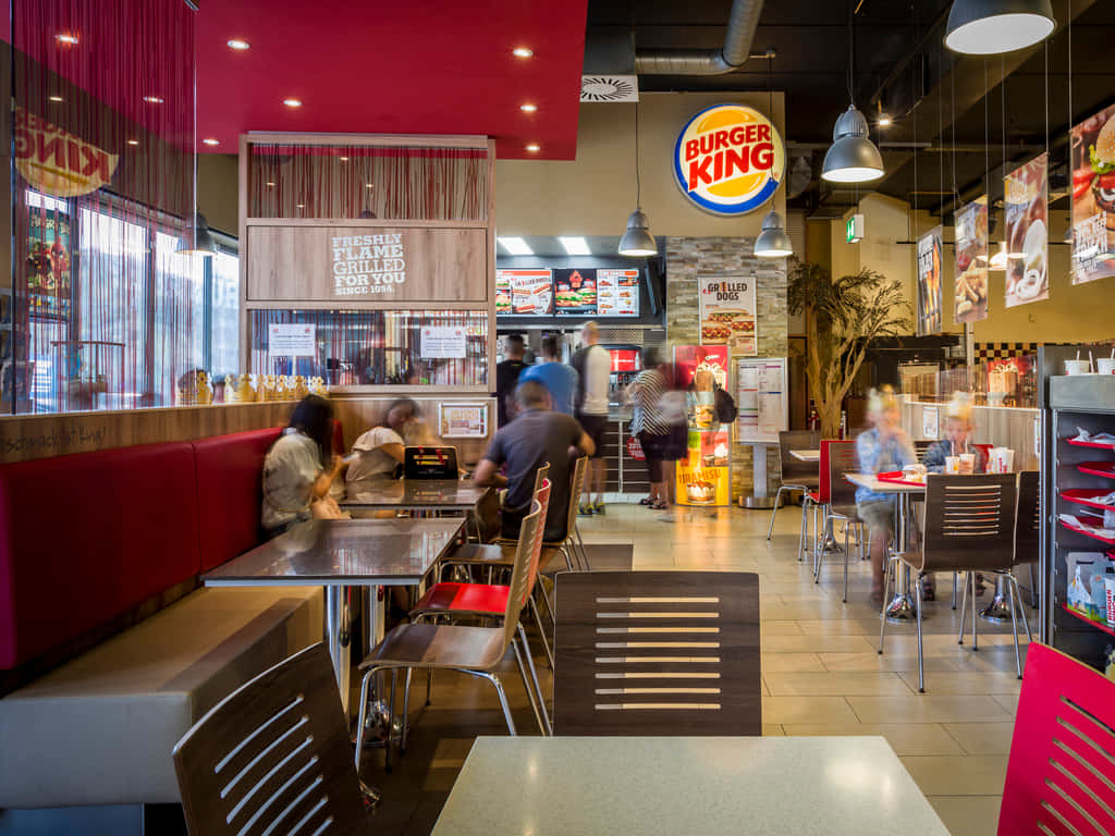 Burger King 桌布 壁紙 — 一間繁忙的Burger King餐廳，設有紅色卡座，顧客在明亮的燈光和品牌標誌下用餐。