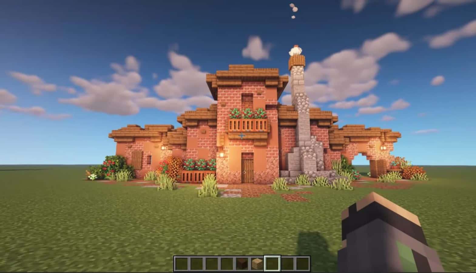 可愛 Minecraft 桌布 壁紙 — 一間舒適的像素風Minecraft房屋，帶有石頭煙囪和花箱，矗立在藍天白雲下的草地上。