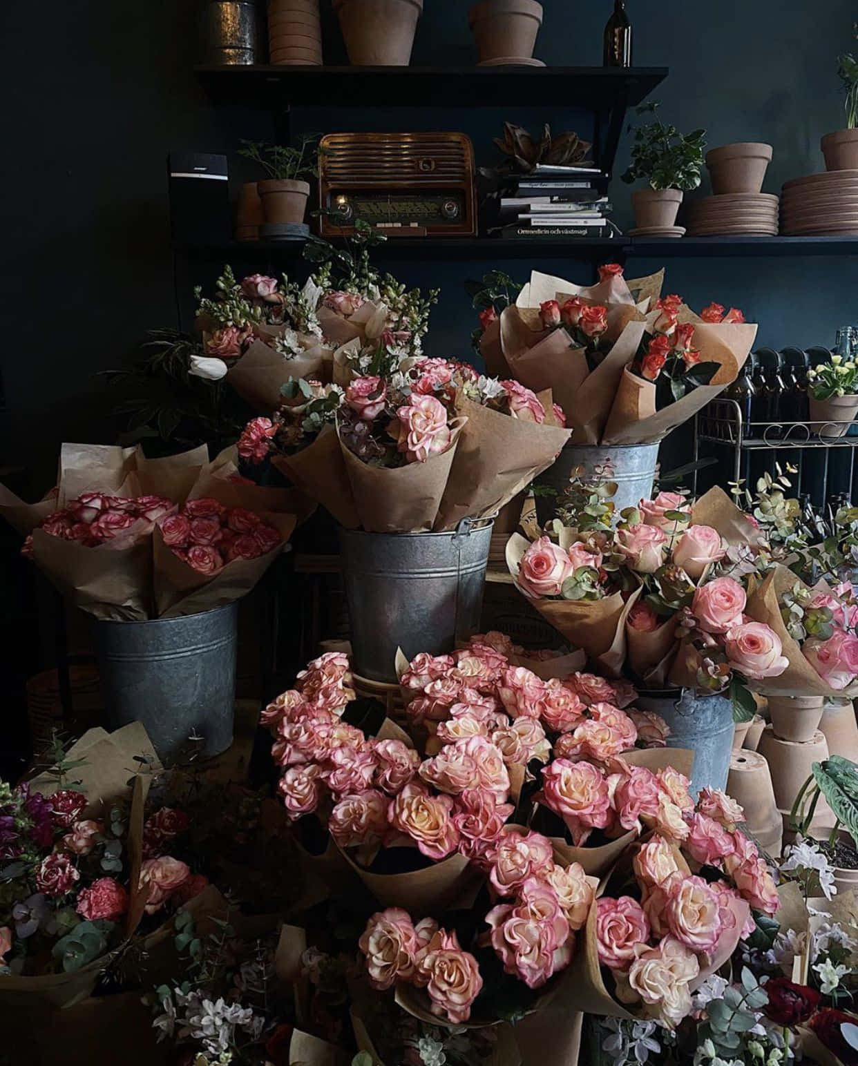 Flower Shop 桌布 壁紙 — 一間舒適的復古花店，在溫暖燈光下，擺滿了放在鄉村風格金屬桶和棕色紙包裝中的粉紅玫瑰。