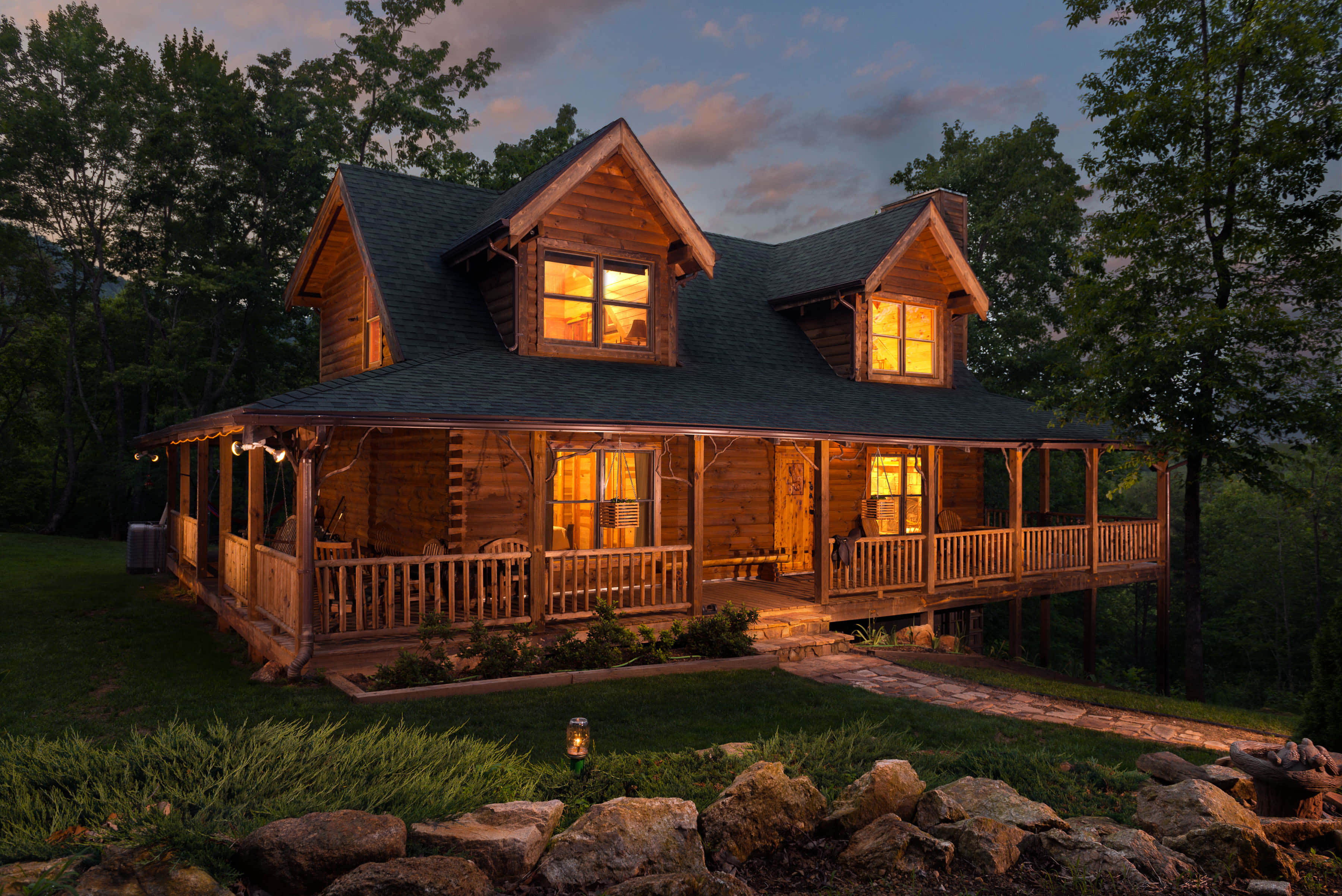 Log Cabin 桌布 壁紙 — 一間舒適的木屋，溫暖發光的窗戶，在黃昏時分 nestled 在樹木之間。