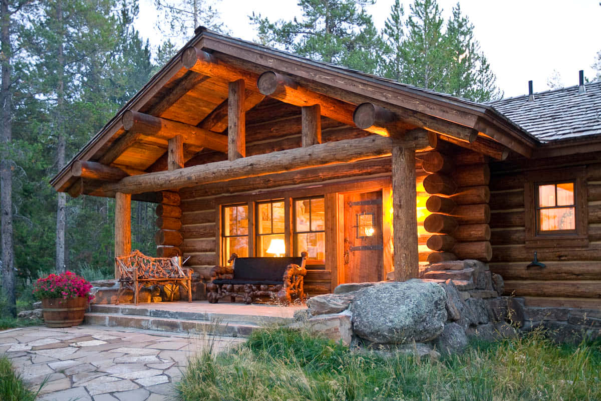 Log Cabin 桌布 壁紙 — 一間舒適的木屋，溫暖的窗戶在黃昏時分閃爍著光芒，坐落在高大的松樹之間。
