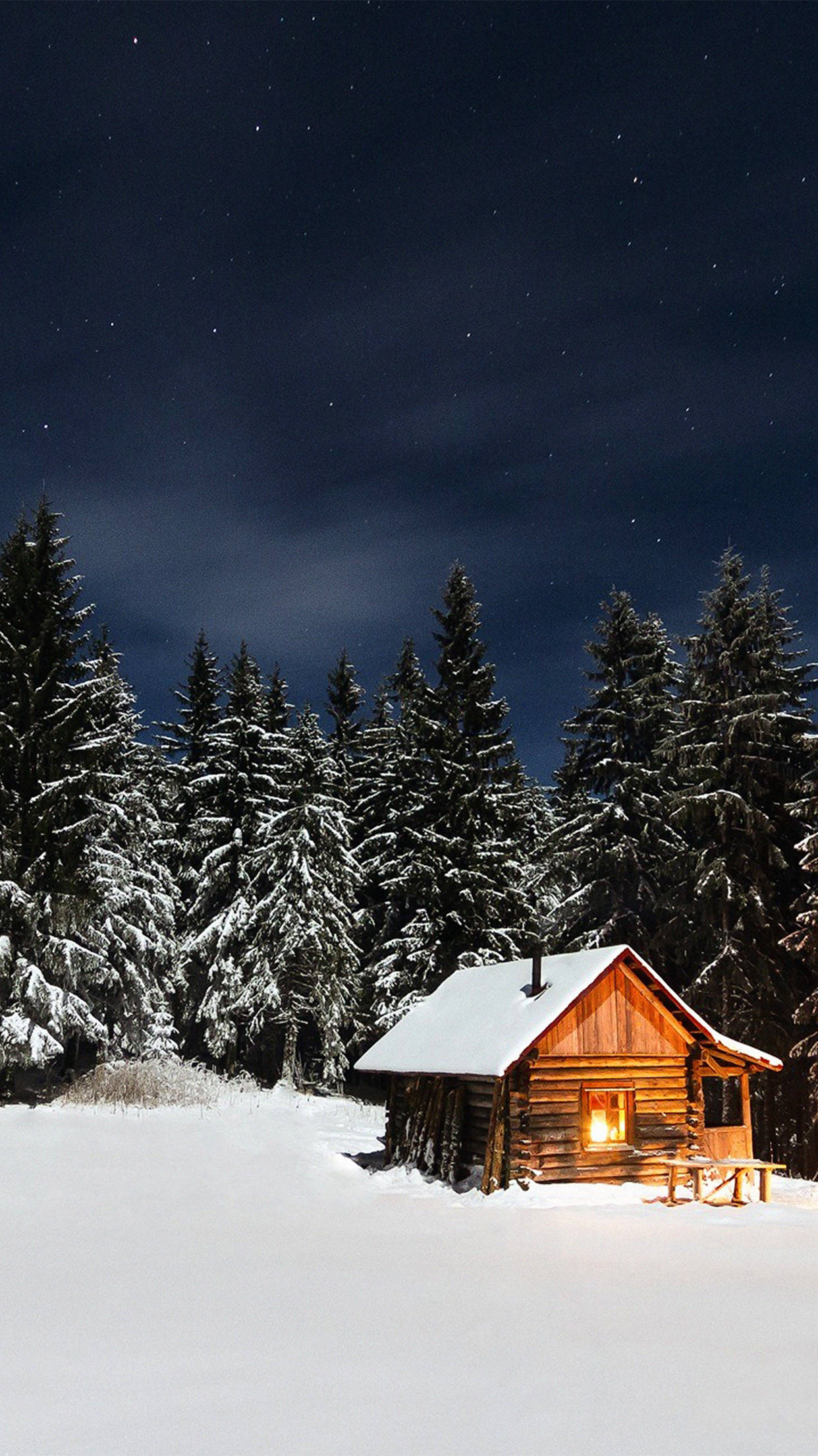 Winter House 桌布 壁紙 — 一間舒適的木屋，窗戶透出光芒，獨自坐落在白雪覆蓋的森林中，上方是繁星點點的夜空。