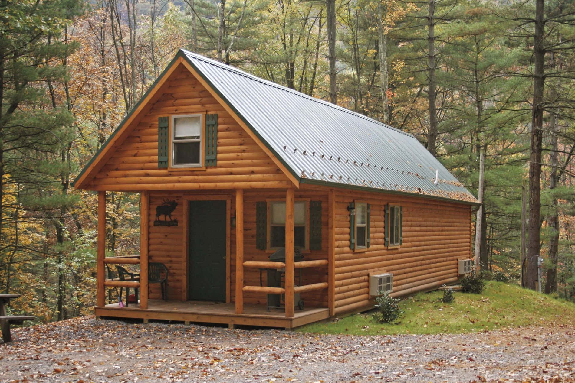 Log Cabin 桌布 壁紙 — 一間舒適的木屋，金屬屋頂，坐落在秋樹之間，金黃的樹葉散落在地上。