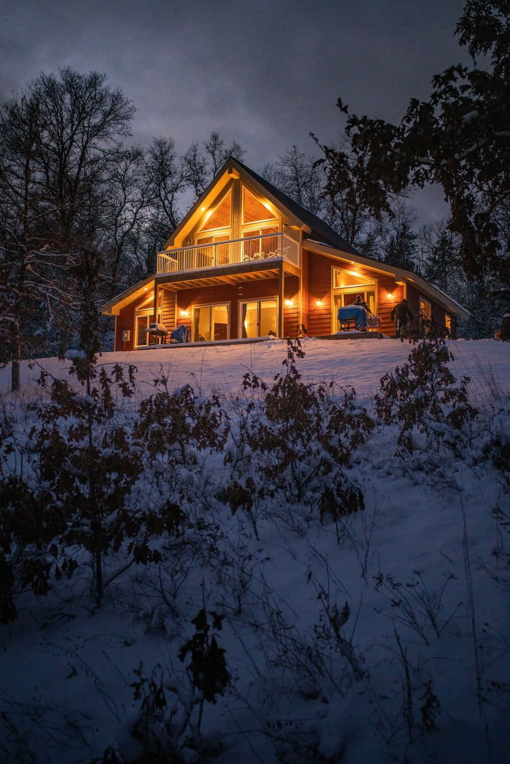 Cozy Winter Cabin 桌布 壁紙 — 一間舒適的木屋在雪暮森林中溫暖地發光，邀請人們在冬日寧靜的懷抱中享受舒適。