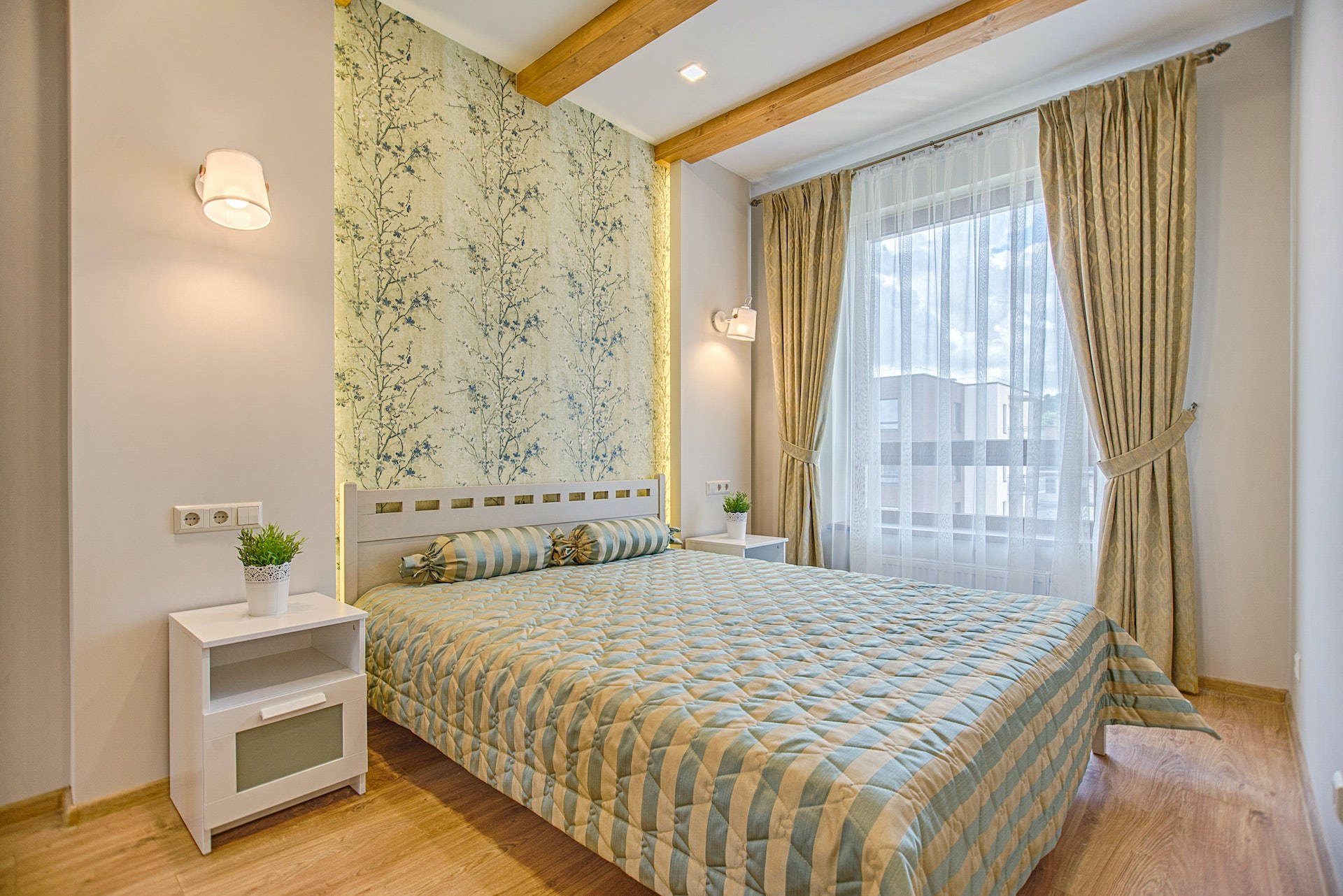 bed 桌布 壁紙 — 一間舒適的臥室，配有絎縫床、花卉壁紙、木樑和讓柔和日光透進的薄紗窗簾。