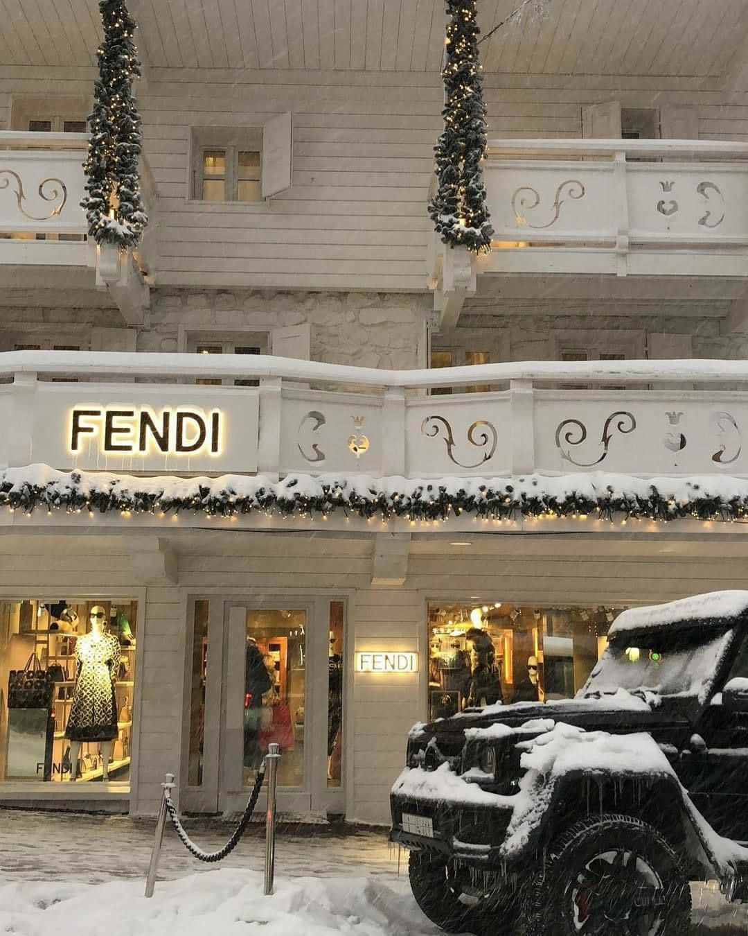 Fendi 桌布 壁紙 — 一間被雪覆蓋的FENDI精品店，帶有節日燈飾，一輛黑色SUV停在外面，冬日天空下。
