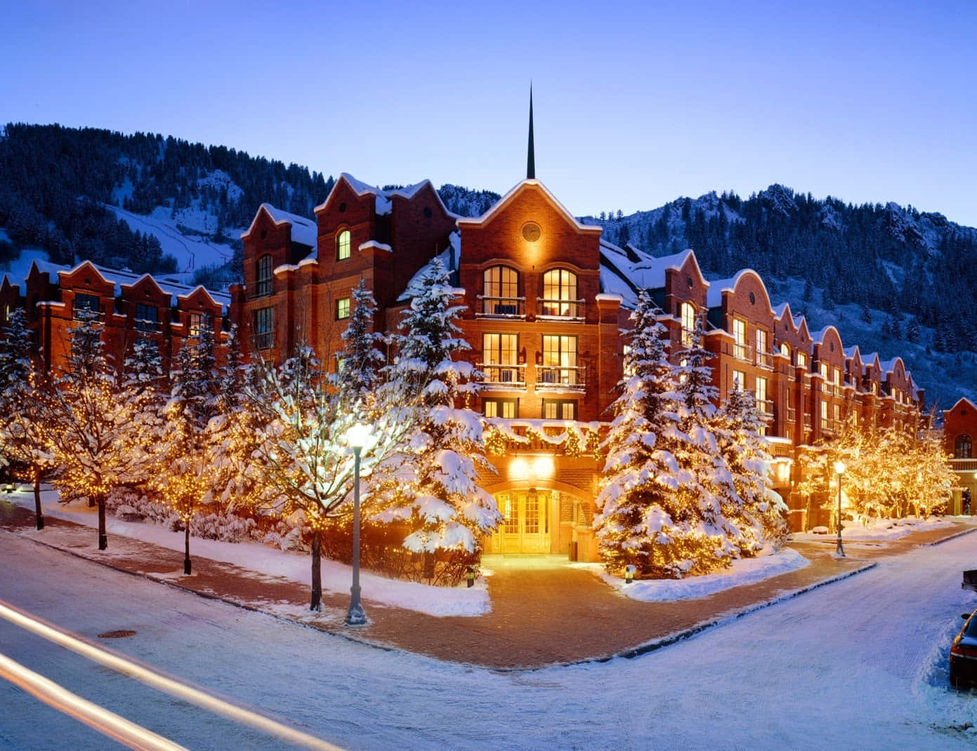 Colorado 桌布 壁紙 — 一間被雪覆蓋的宏偉磚砌酒店，在暮色山景中散發溫暖光芒，周圍樹木燈光璀璨。