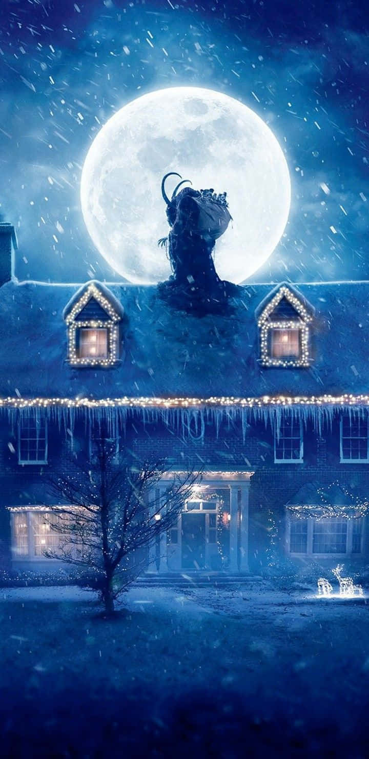 Krampus 桌布 壁紙 — 一間被雪覆蓋的房屋，窗戶發光，屋簷掛著冰柱，在巨大的滿月下，屋頂上有一個帶角的人物剪影。