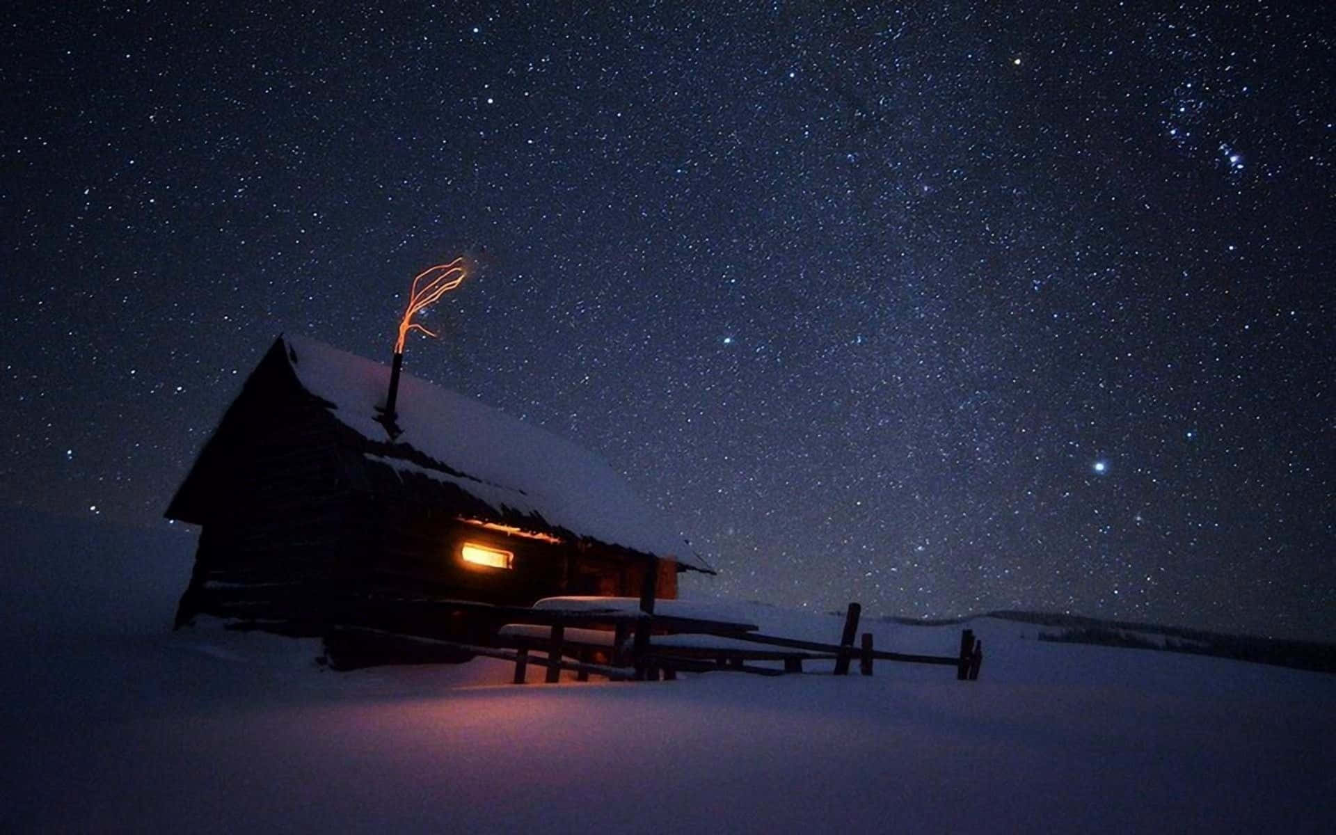 桌布 壁紙 — 一間被雪覆蓋的木屋在星空的冬夜下溫暖地發光，煙囪亮著。