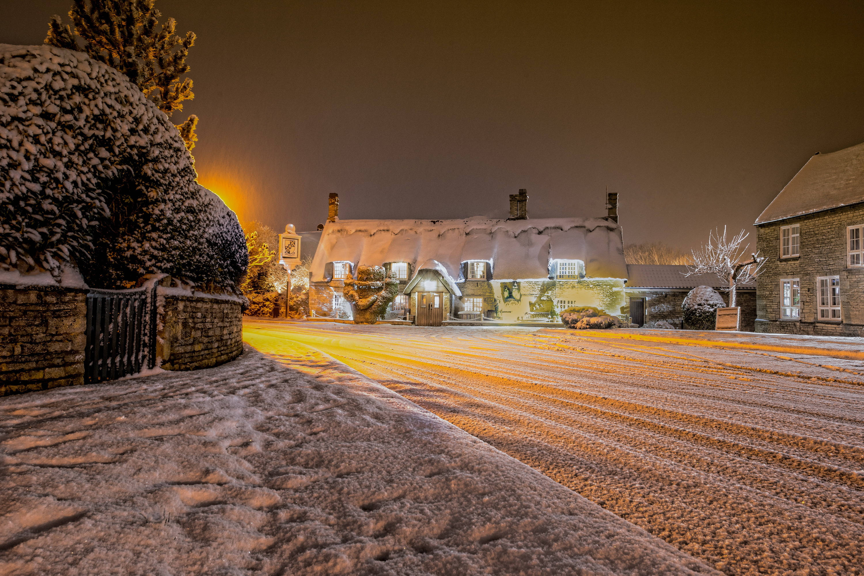 England 桌布 壁紙 — 一間被雪覆蓋的村莊房屋在寧靜的冬夜裡，在街燈下散發著溫暖的光芒。