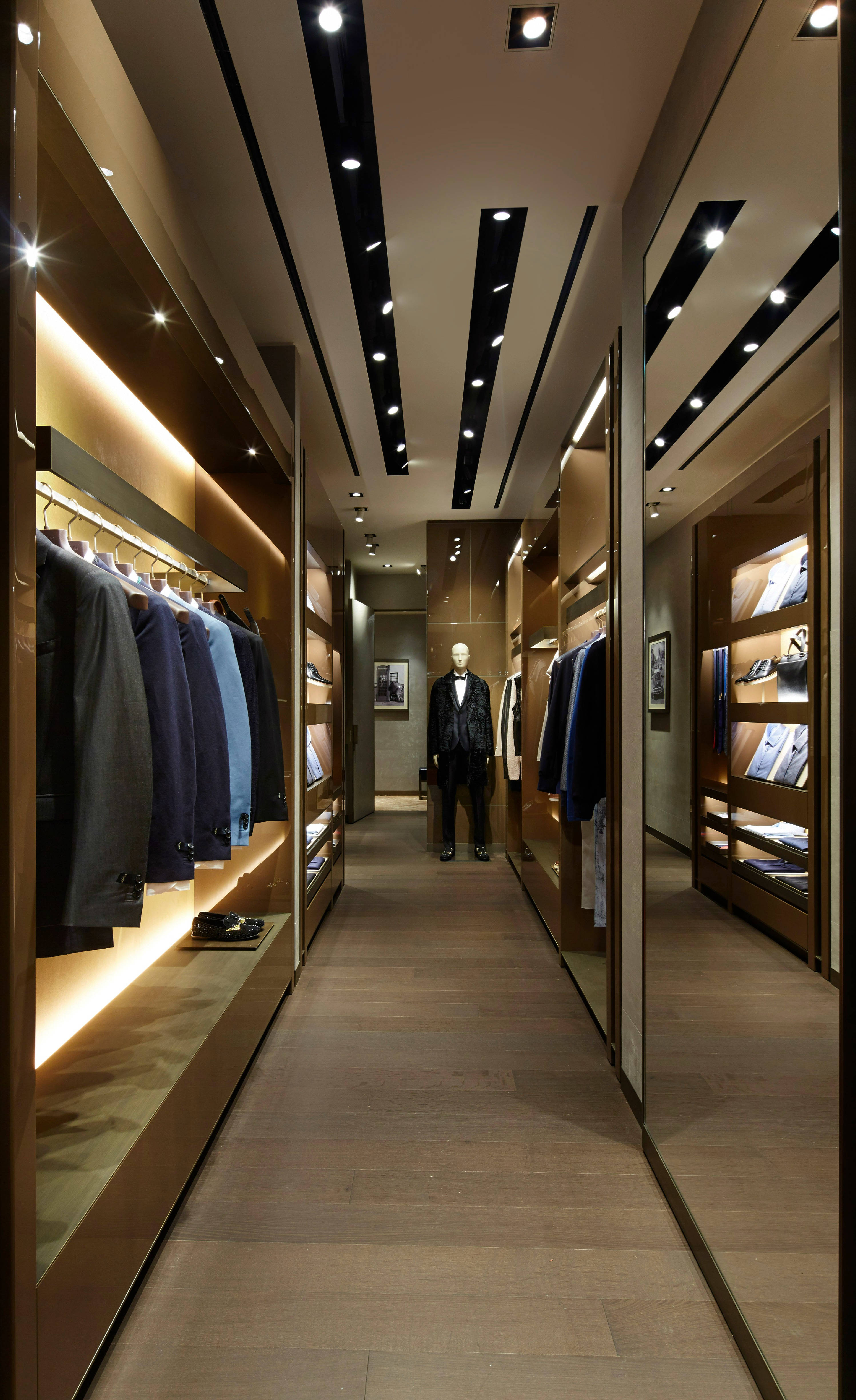 Fendi 桌布 壁紙 — 一間豪華現代男士服裝精品店，配有溫暖燈光、木質貨架，以及走廊盡頭穿著西裝的人體模型。