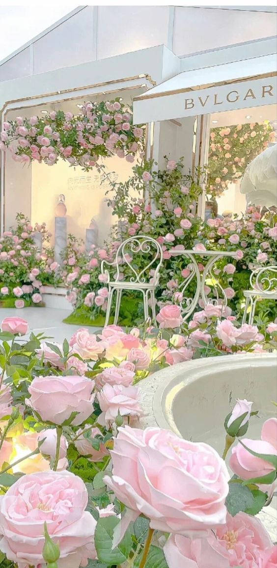 Pink Vintage Aesthetic 桌布 壁紙 — 一間豪華的戶外精品店，在柔和日光下裝飾著層疊的粉紅玫瑰和白色鍛鐵家具。