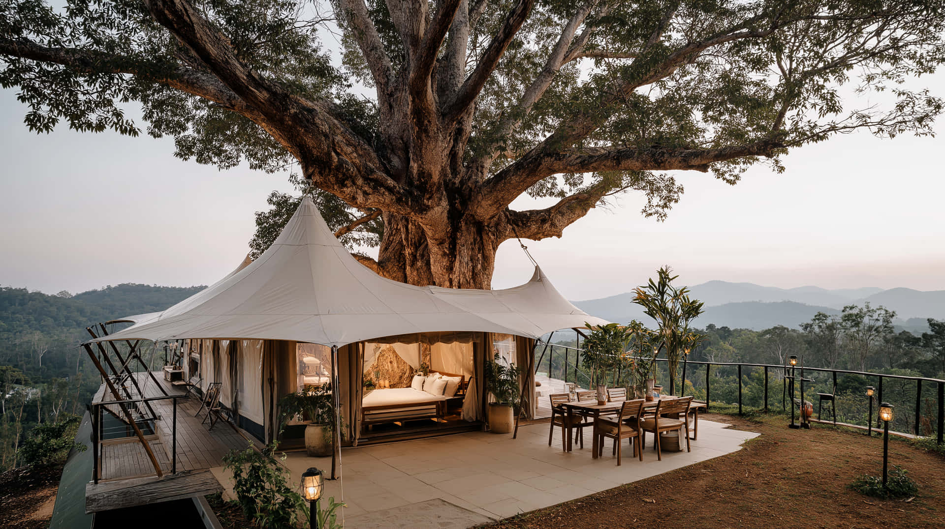 Luxurious Glamping Resort Under a Grand Ancient Tree 壁紙 — 一間豪華的白色帳篷套房，坐落在一棵大樹下，設有木質露台和用餐區，可俯瞰黃昏時分起伏的丘陵。