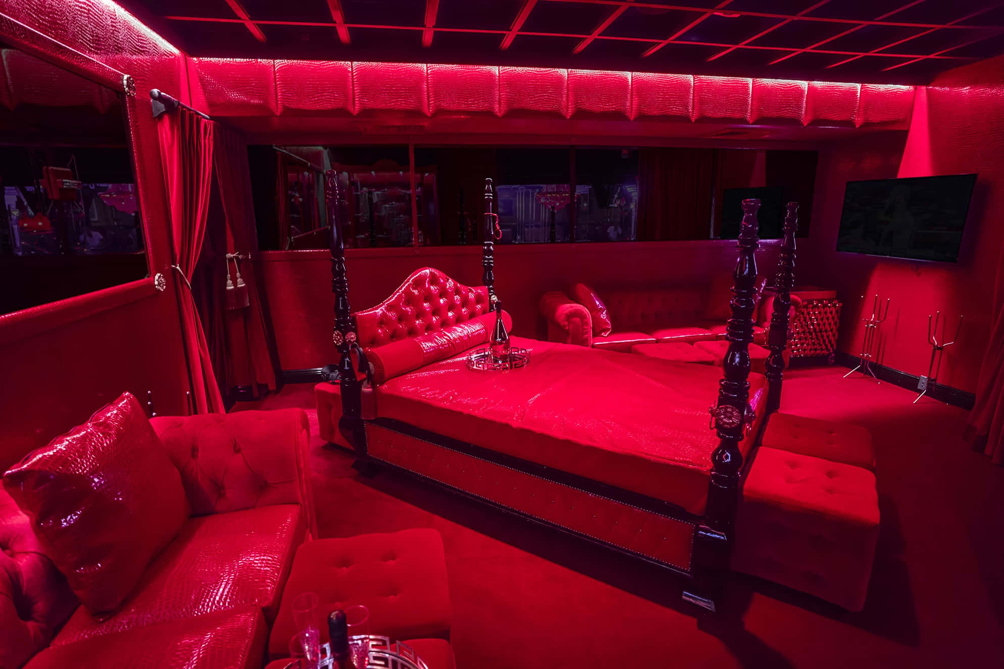 Red Room 桌布 壁紙 — 一間豪華的臥室沐浴在強烈的紅光中，設有一張帶簇絨皮革和深色木柱的四柱床，周圍環繞著相配的紅色家具。