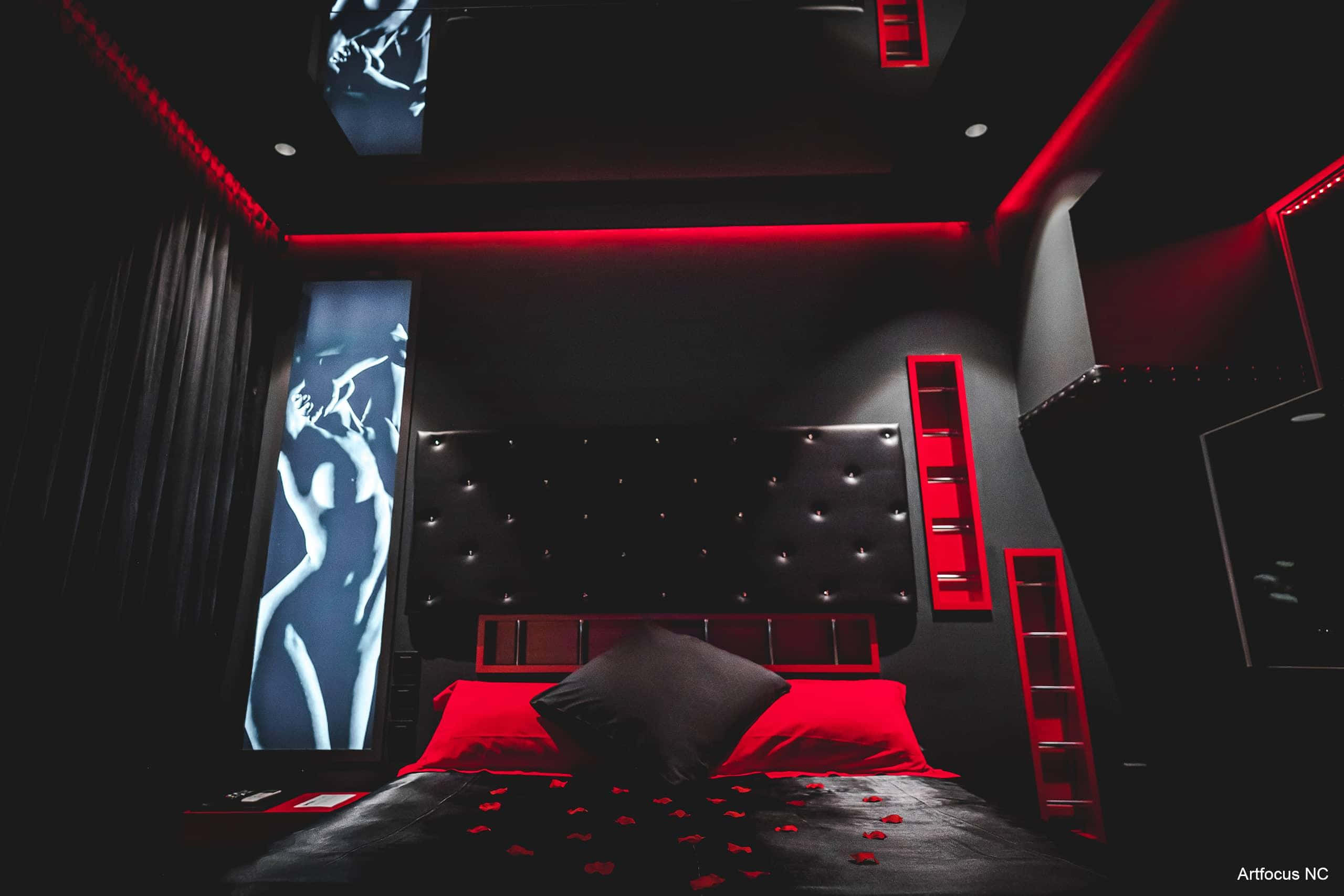 Red Room 桌布 壁紙 — 一間豪華臥室，沐浴在戲劇性的紅光中，配有一張黑色簇絨床、玫瑰花瓣和發光的牆壁壁畫。
