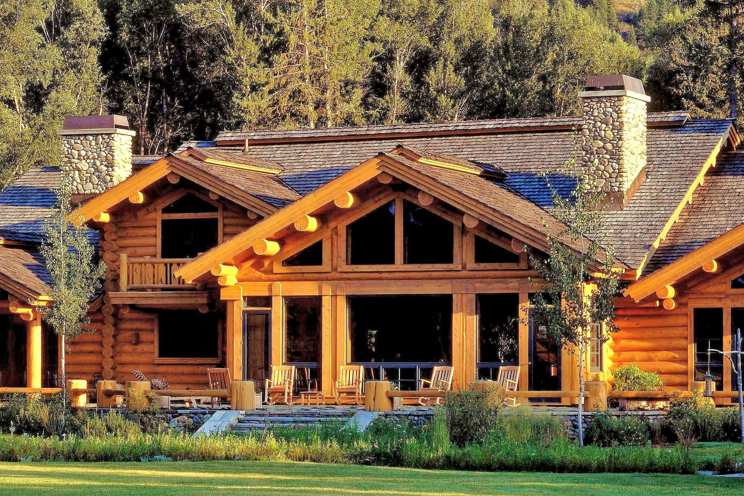 Log Cabin 桌布 壁紙 — 一間質樸的木屋，配有石砌煙囪和木製門廊，坐落在陽光明媚的森林空地中。