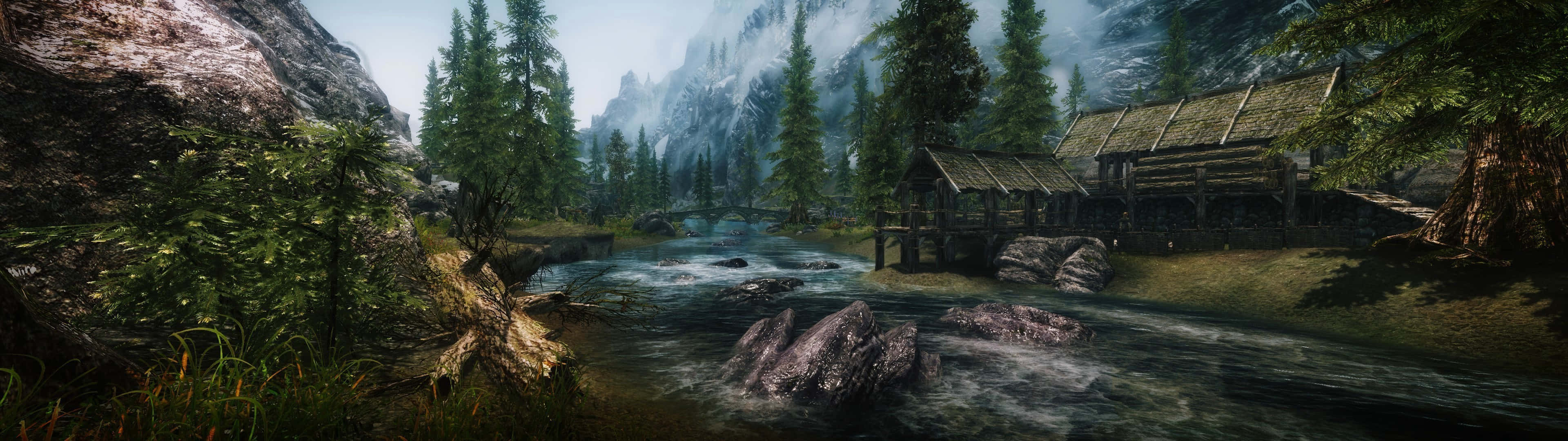 Skyrim Landscape 桌布 壁紙 — 一間質樸的木屋坐落在霧氣瀰漫的山林之中，旁邊是一條湍急的河流，周圍有高聳的常青樹和岩石河岸。