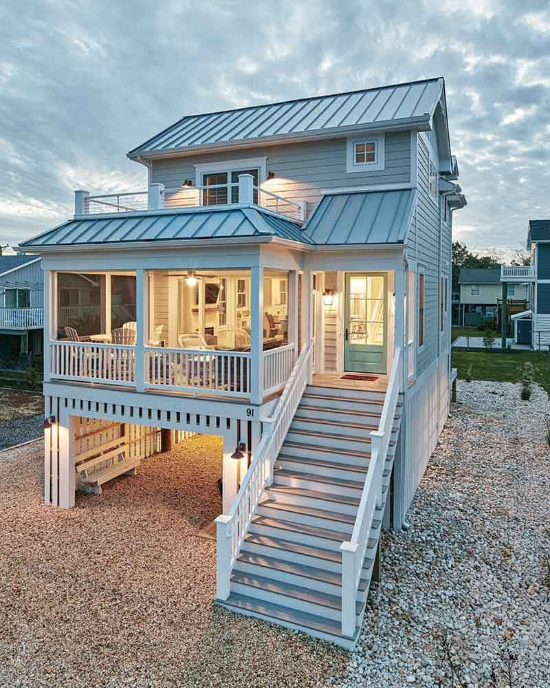 Cottage 桌布 壁紙 — 一間迷人的兩層海灘別墅，擁有金屬屋頂和發光的窗戶，矗立在碎石地上，天空佈滿雲層的暮色中。