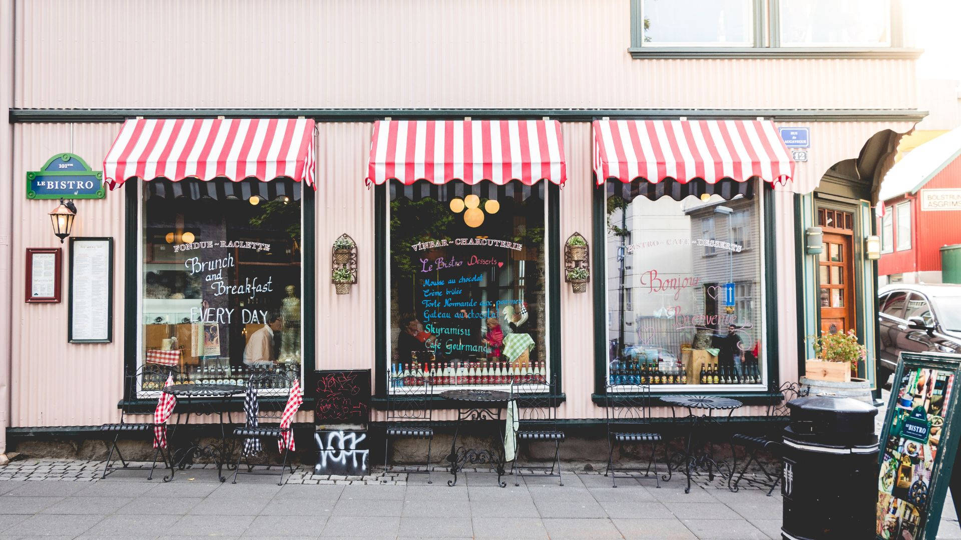 Store 桌布 壁紙 — 一間迷人的小餐館，設有紅白條紋遮陽篷和戶外餐桌，靜靜地坐落在寧靜的街道上，令人心動。