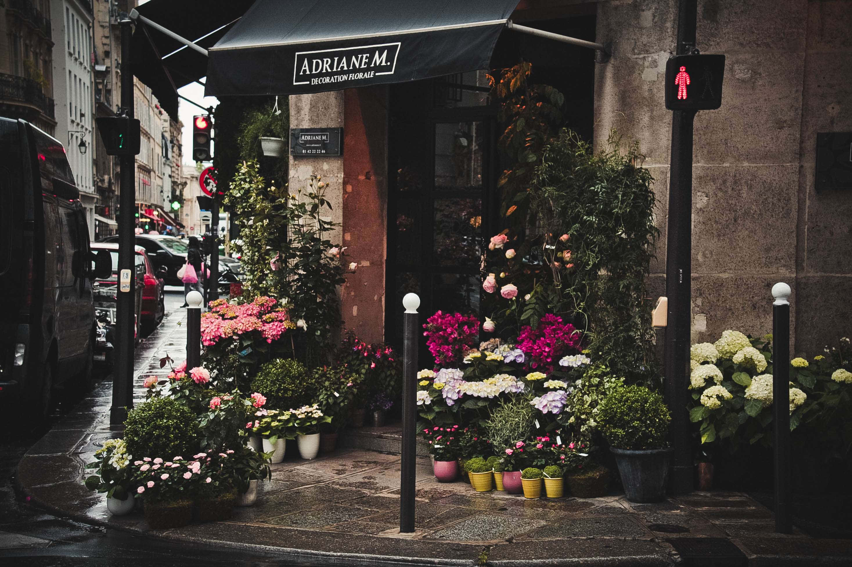 Flower Shop 桌布 壁紙 — 一間迷人的歐洲花店，在雨天的城市街道上，黑色遮陽篷下綻放著色彩繽紛的花朵。