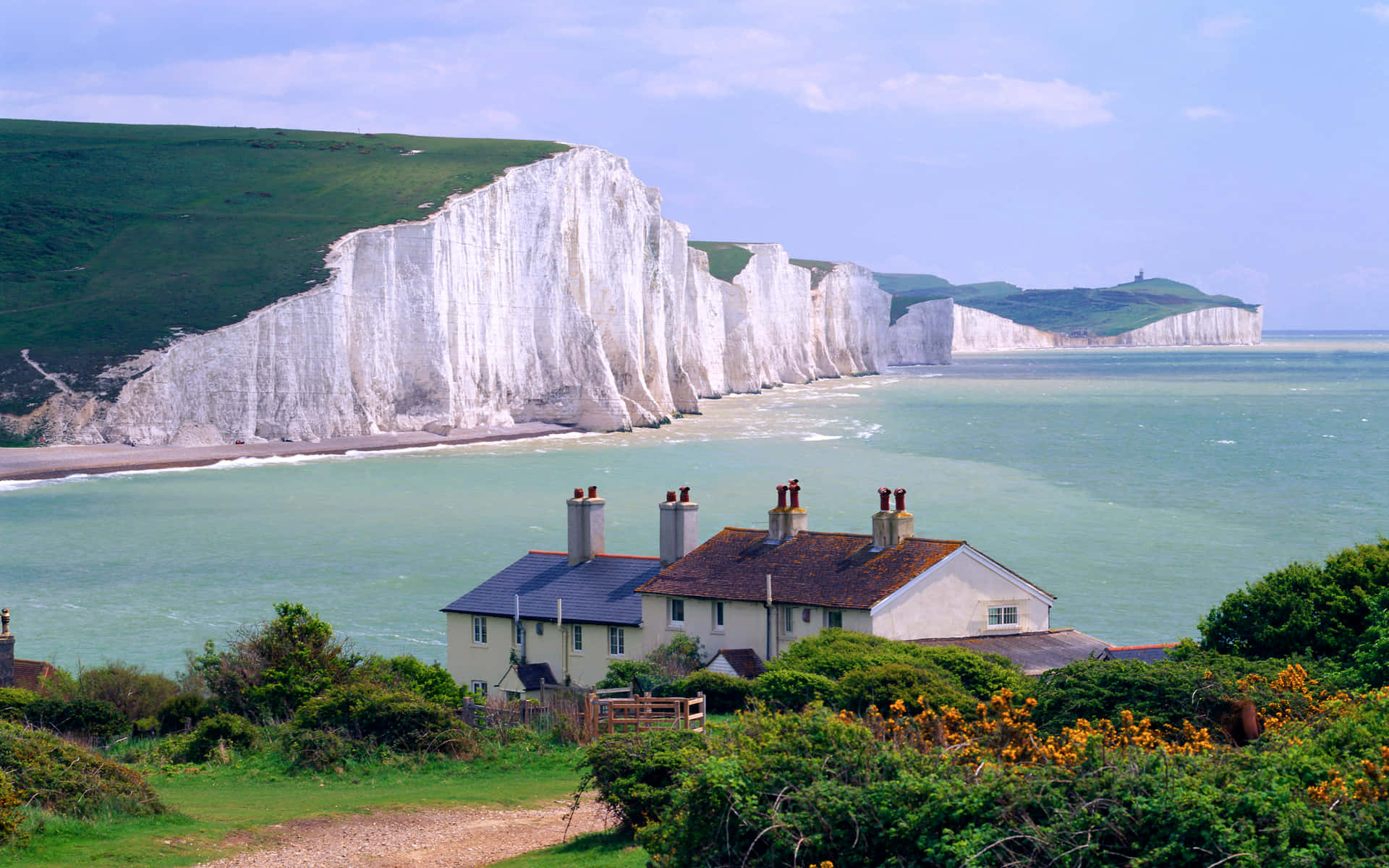 England 桌布 壁紙 — 一間迷人的海岸小屋，隱藏在綠意之中，背景是戲劇性的白色白堊懸崖和碧綠色的海洋。