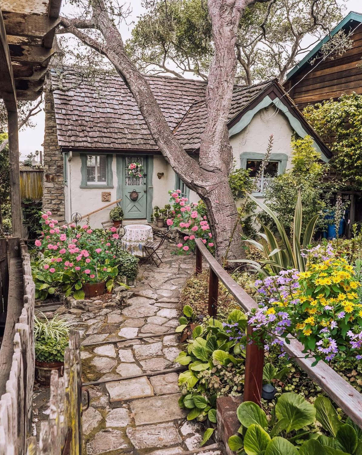 一間古樸的石頭小屋，周圍環繞著色彩繽紛的花朵和一條石徑。 — 田園風 GIF 壁紙