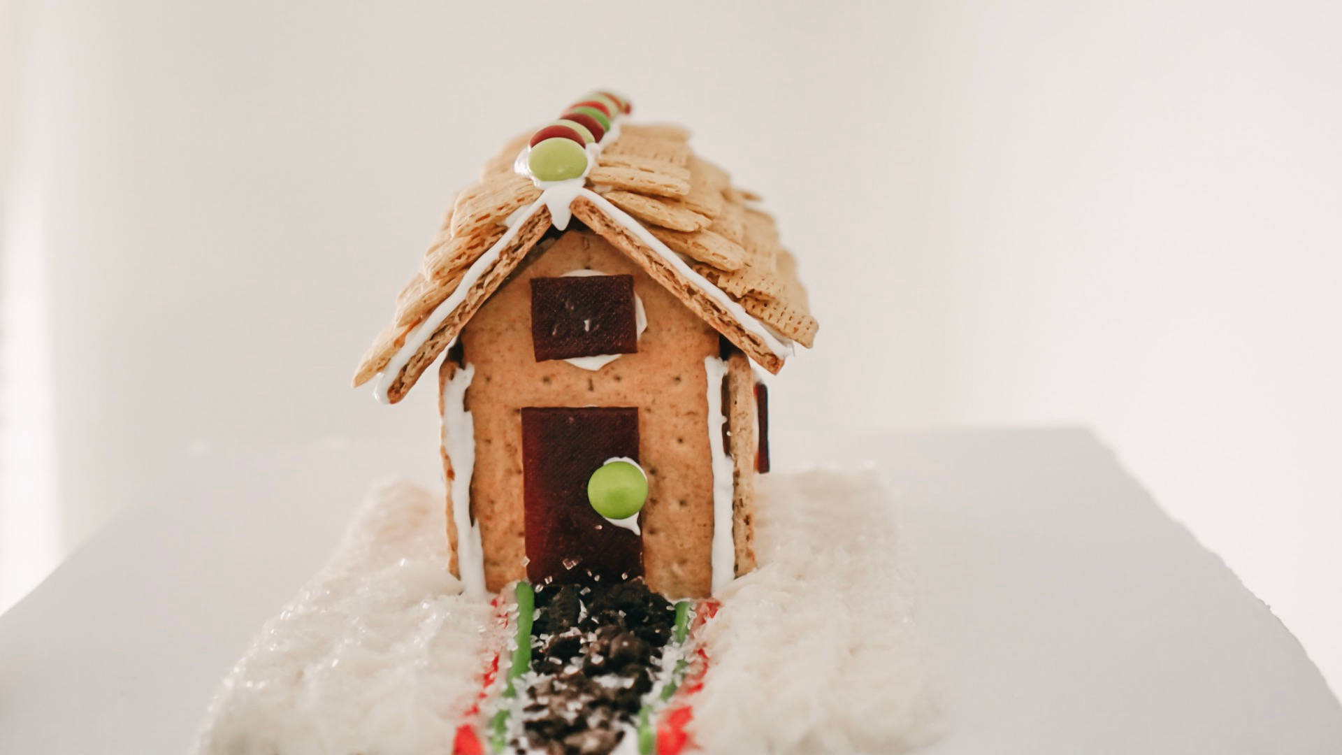 Gingerbread House 桌布 壁紙 — 一間迷人的薑餅屋，帶有全麥餅乾屋頂和糖果裝飾，坐落在雪白的糖粉中。
