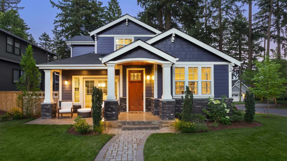 Nice Houses 桌布 壁紙 — 一間迷人的藍色房子，帶有白色飾邊和發光的窗戶，在黃昏時分歡迎您，周圍環繞著高大的樹木和一條石徑。