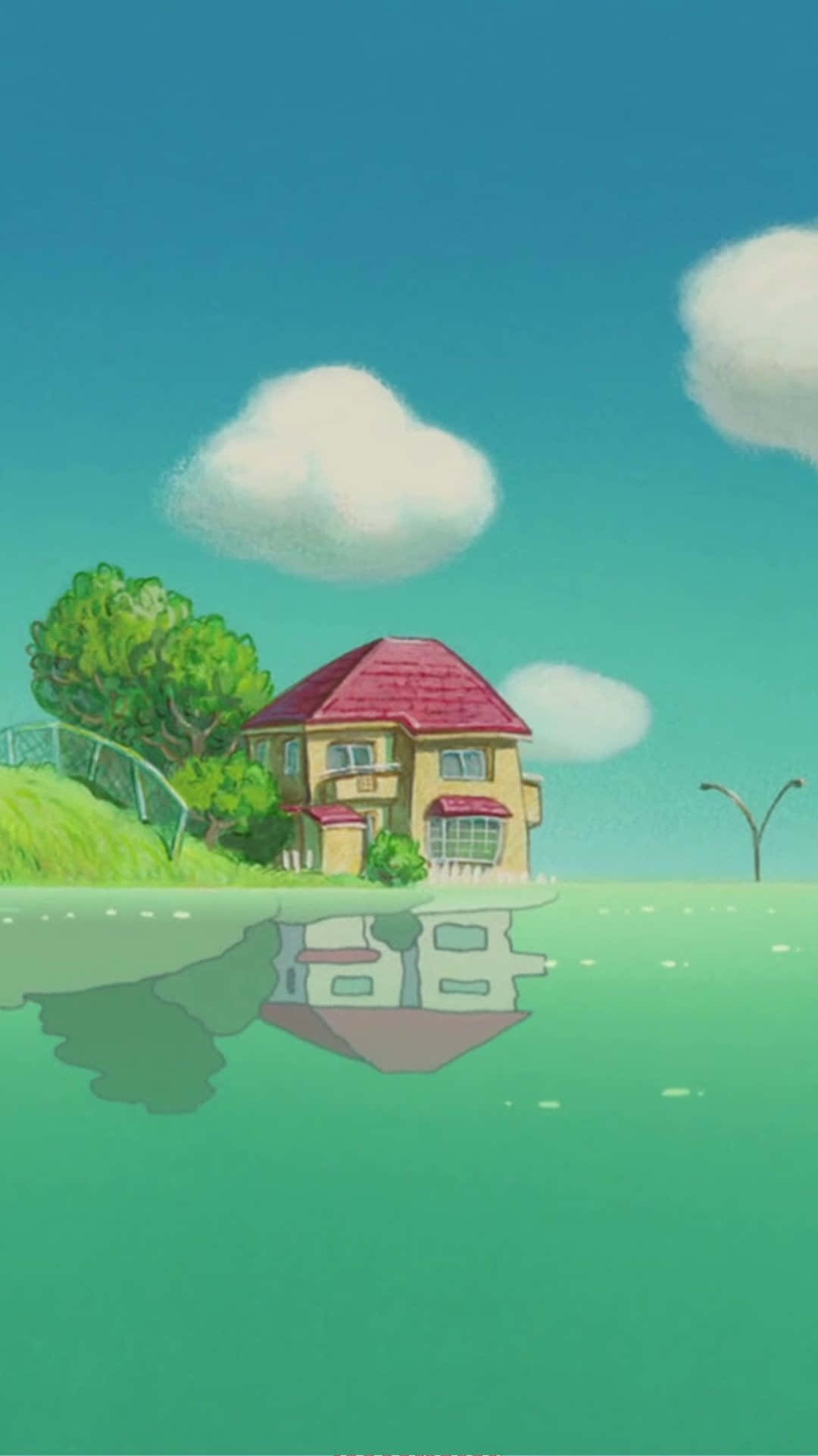 Studio Ghibli Phone 桌布 壁紙 — 一間迷人的黃色房子，紅色屋頂，坐落在長滿草的山丘上，旁邊是平靜的綠色水面，在晴朗的藍天下有蓬鬆的白雲。